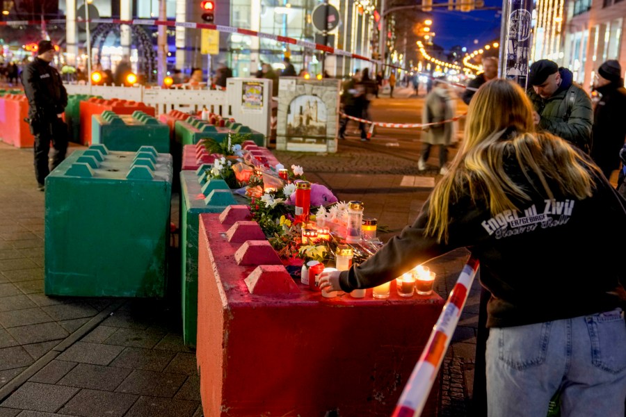 People lay flowers and light candles on concrete blocks that protect the Christmas market in Magdeburg, Germany, Saturday, Dec. 21, 2024, where a car drove into a crowd on Friday evening. (AP Photo/Michael Probst)