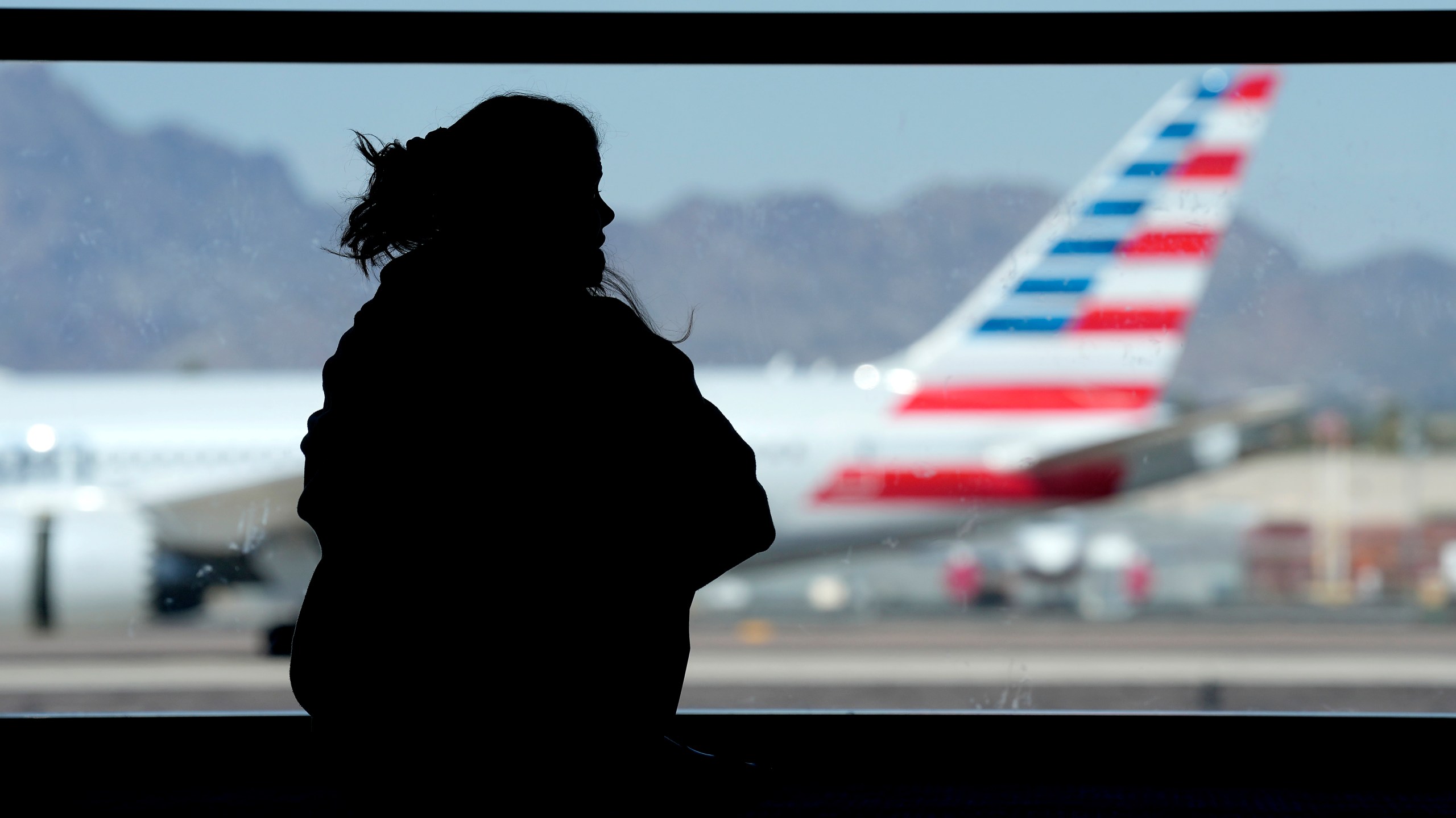 FILE - A woman waits for her flight as an American Airlines jet passes by at Sky Harbor airport on March 4, 2023, in Phoenix. (AP Photo/Charlie Riedel, File)