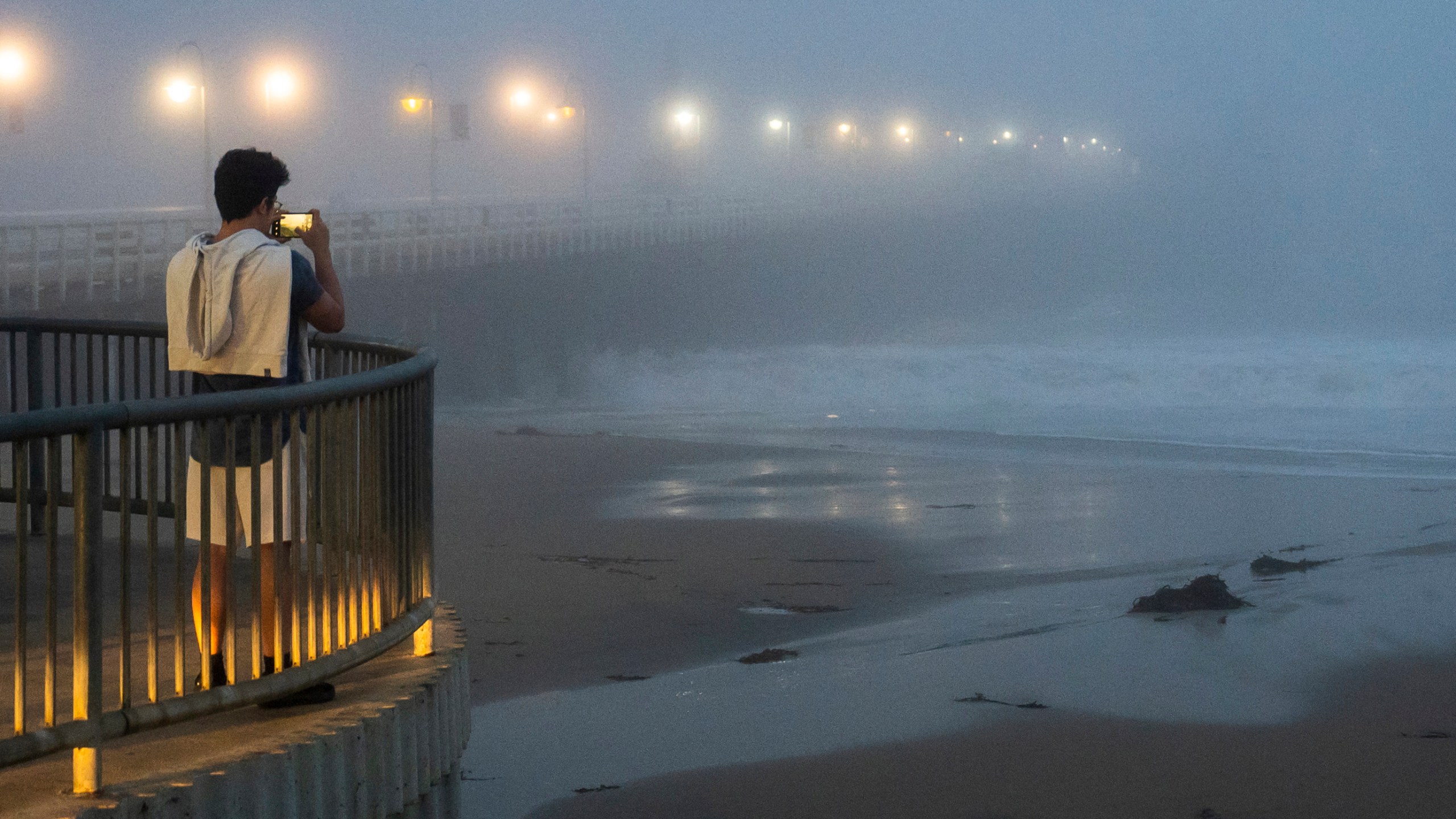 A person takes a photo of high surf near the Santa Cruz Wharf in Santa Cruz, Calif., Monday, Dec. 23, 2024. (AP Photo/Nic Coury)