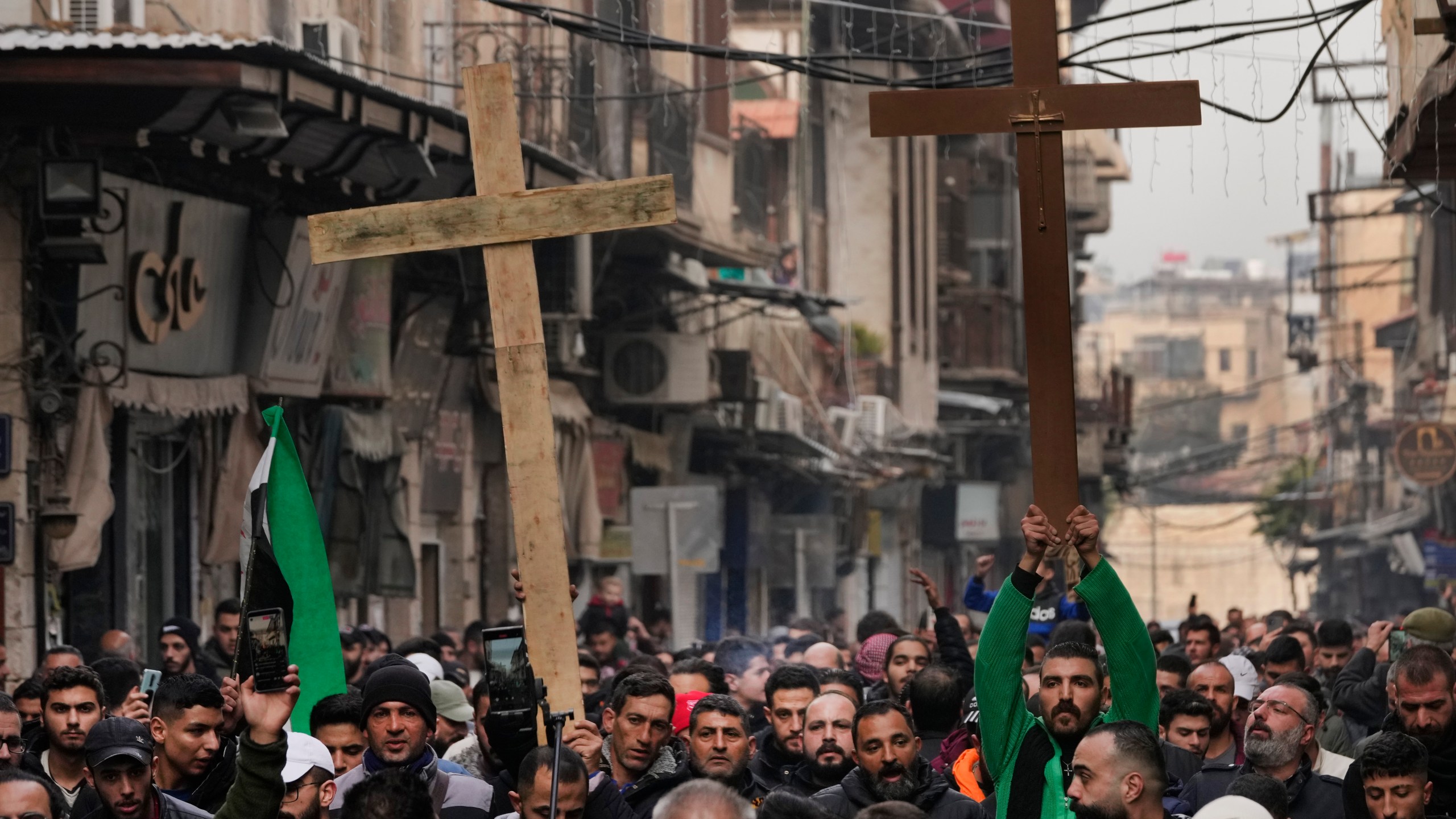 Syrian Christians hold up crosses and shout slogans in Damascus, Syria, Tuesday, Dec. 24, 2024 as they march during a protest after a Christmas tree was set on fire in Hamah city on Sunday. (AP Photo/Hussein Malla)