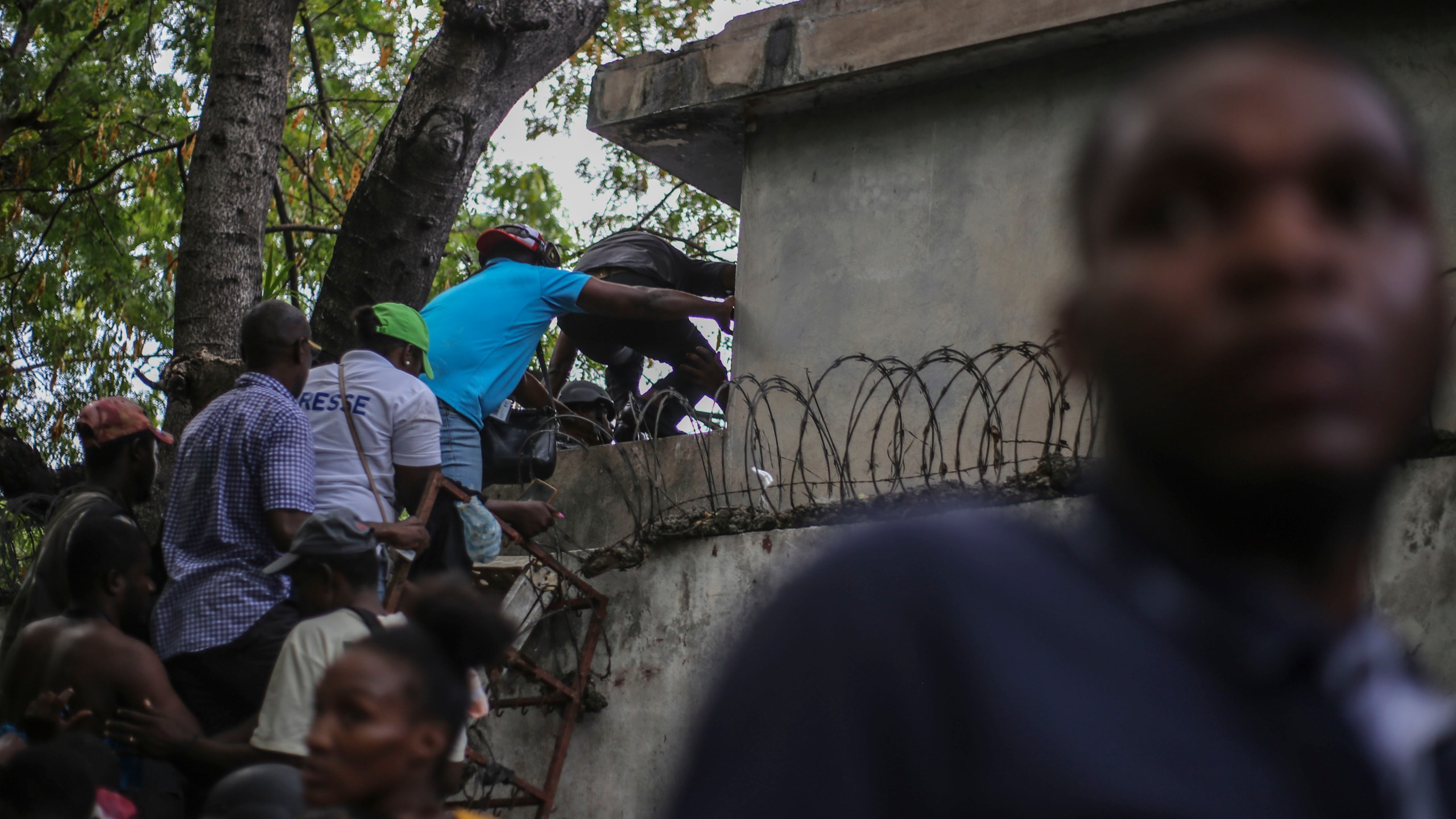 Journalists climb up a wall to take cover from gunfire, after being shot at by armed gangs at the General Hospital in Port-au-Prince, Haiti, Tuesday, Dec. 24, 2024. (AP Photo/Jean Feguens Regala)