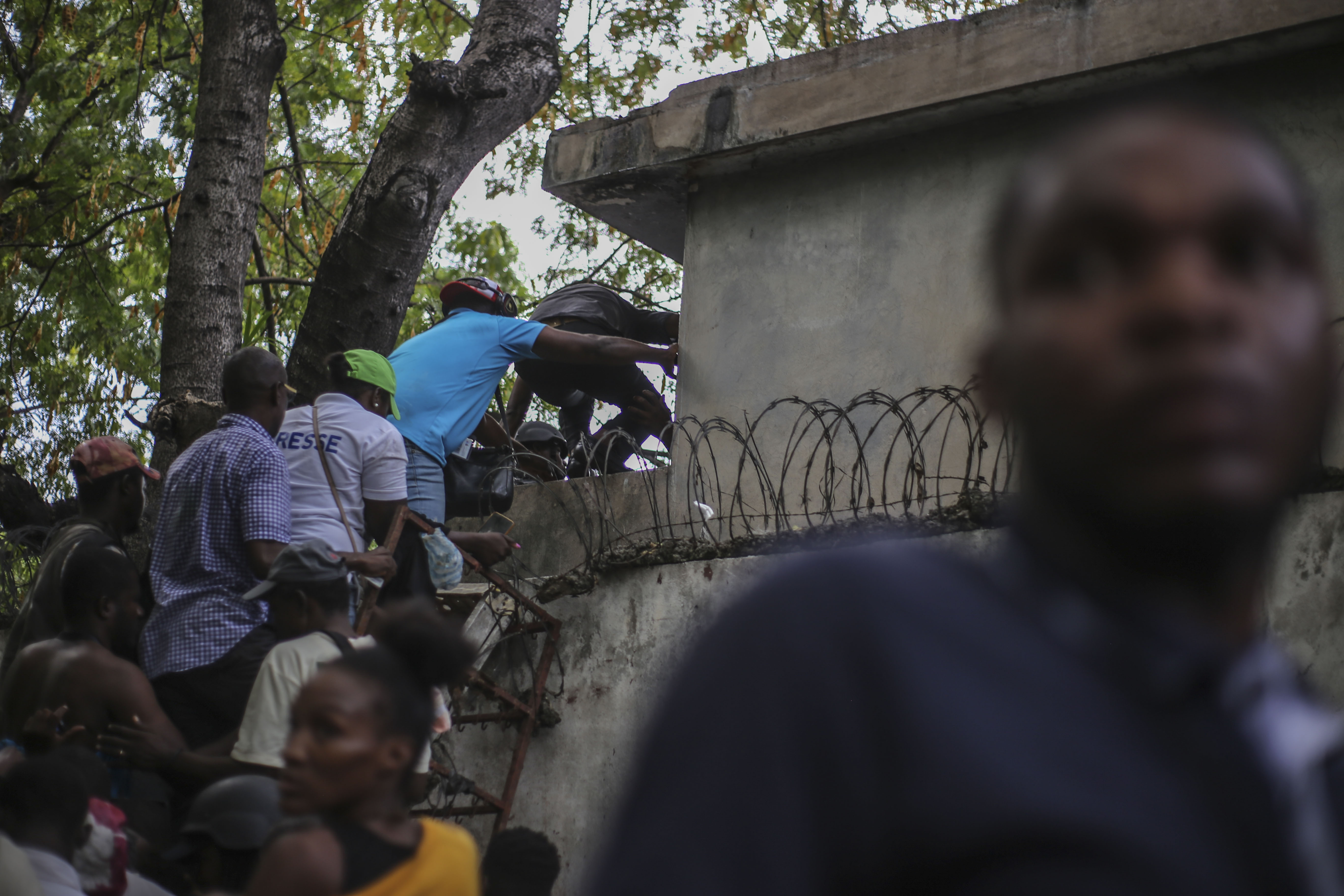 Journalists climb up a wall to take cover from gunfire, after being shot at by armed gangs at the General Hospital in Port-au-Prince, Haiti, Tuesday, Dec. 24, 2024. (AP Photo/Jean Feguens Regala)