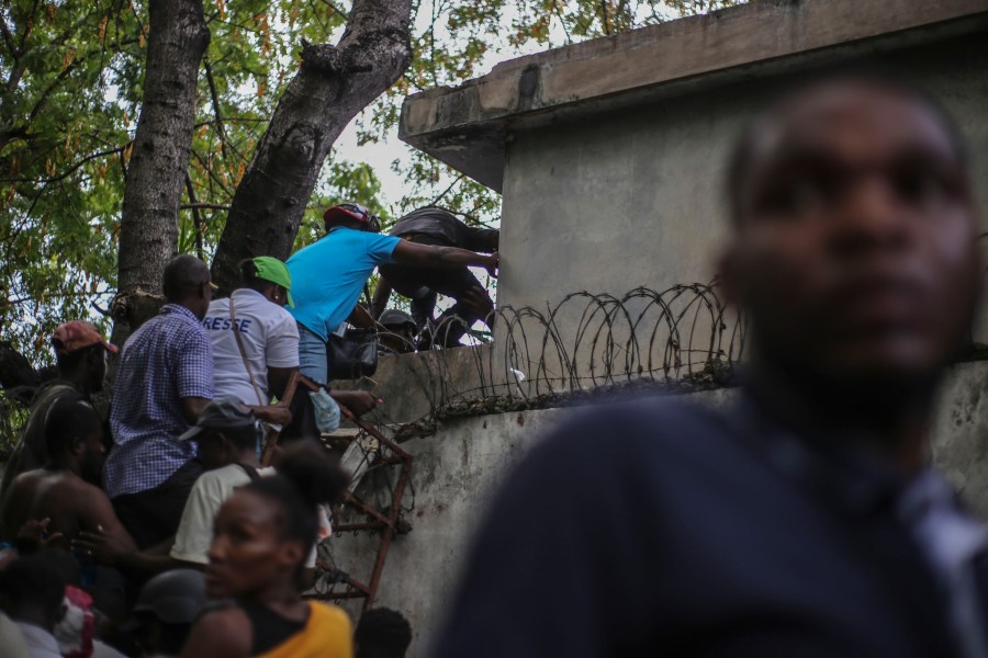 Journalists climb up a wall to take cover from gunfire, after being shot at by armed gangs at the General Hospital in Port-au-Prince, Haiti, Tuesday, Dec. 24, 2024. (AP Photo/Jean Feguens Regala)