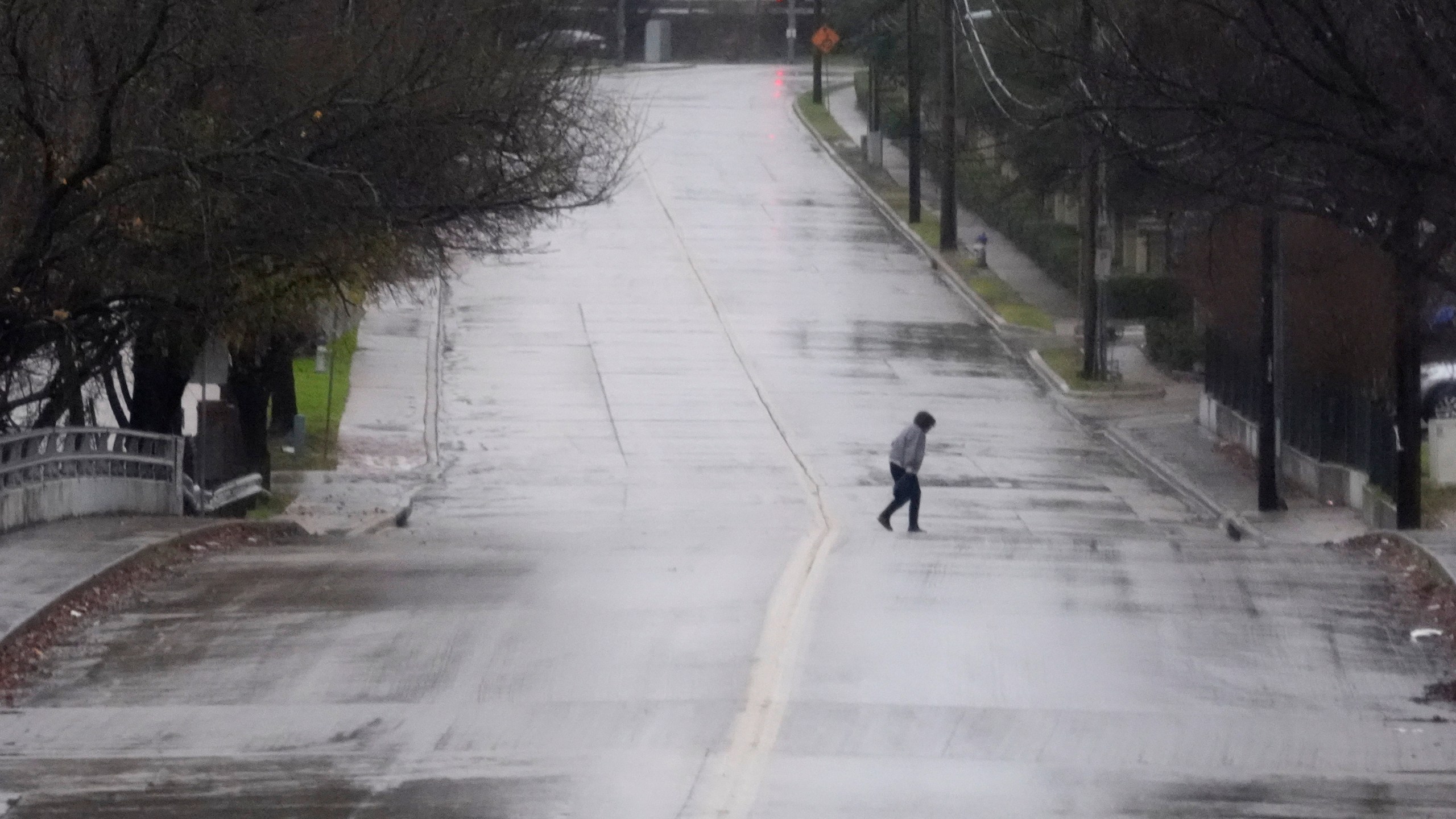 A pedistrian walks across a rain soaked street in Dallas, Thursday, Dec. 26, 2024. (AP Photo/LM Otero)