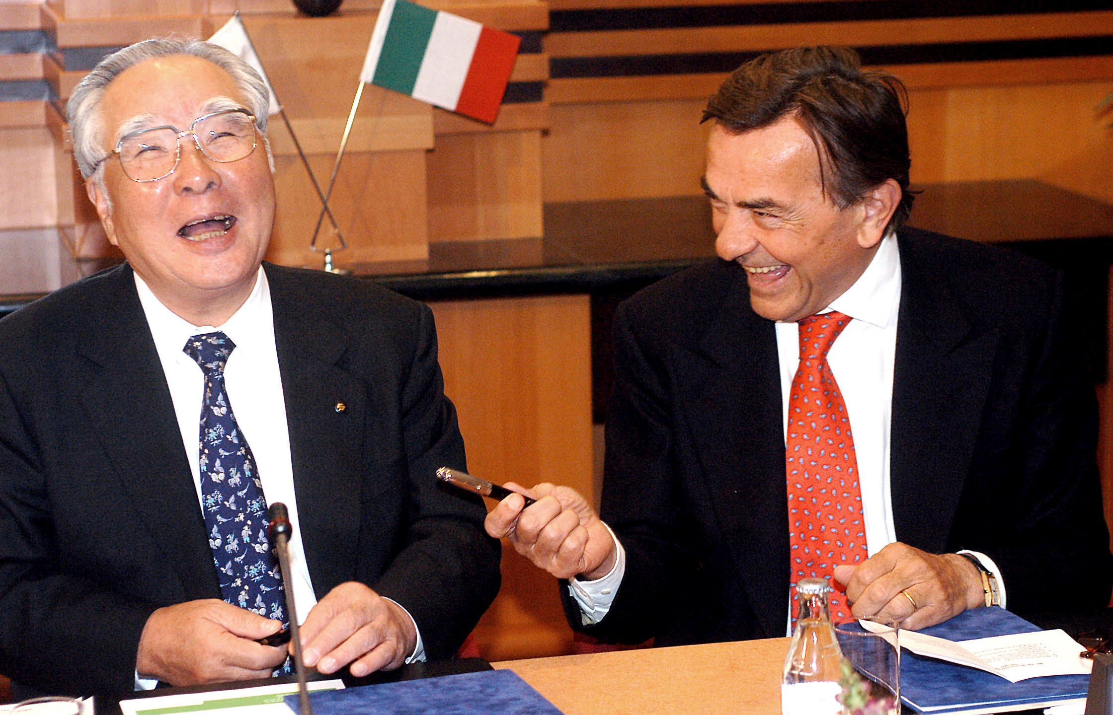 FILE - Chairman and CEO of the Japanese carmaker Suzuki Motor Corp., Osamu Suzuki, left, and President and CEO of Fiat Auto S.p.A. of Italy, Giancarlo Boschetti, share a laugh before they signed an agreement on jointly developing and producing a new sport utility vehicle in a hotel in Budapest, Hungary, April 10, 2003. (Tamas Kovacs/MTI via AP, File)