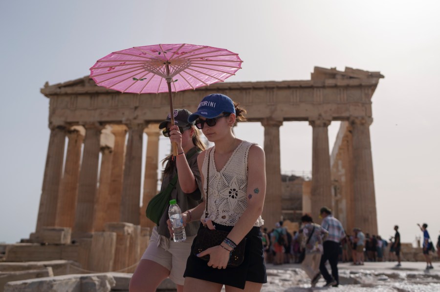 FILE - Tourists with an umbrella walk in front of the Parthenon at the ancient Acropolis in central Athens, June 12, 2024. (AP Photo/Petros Giannakouris, File)