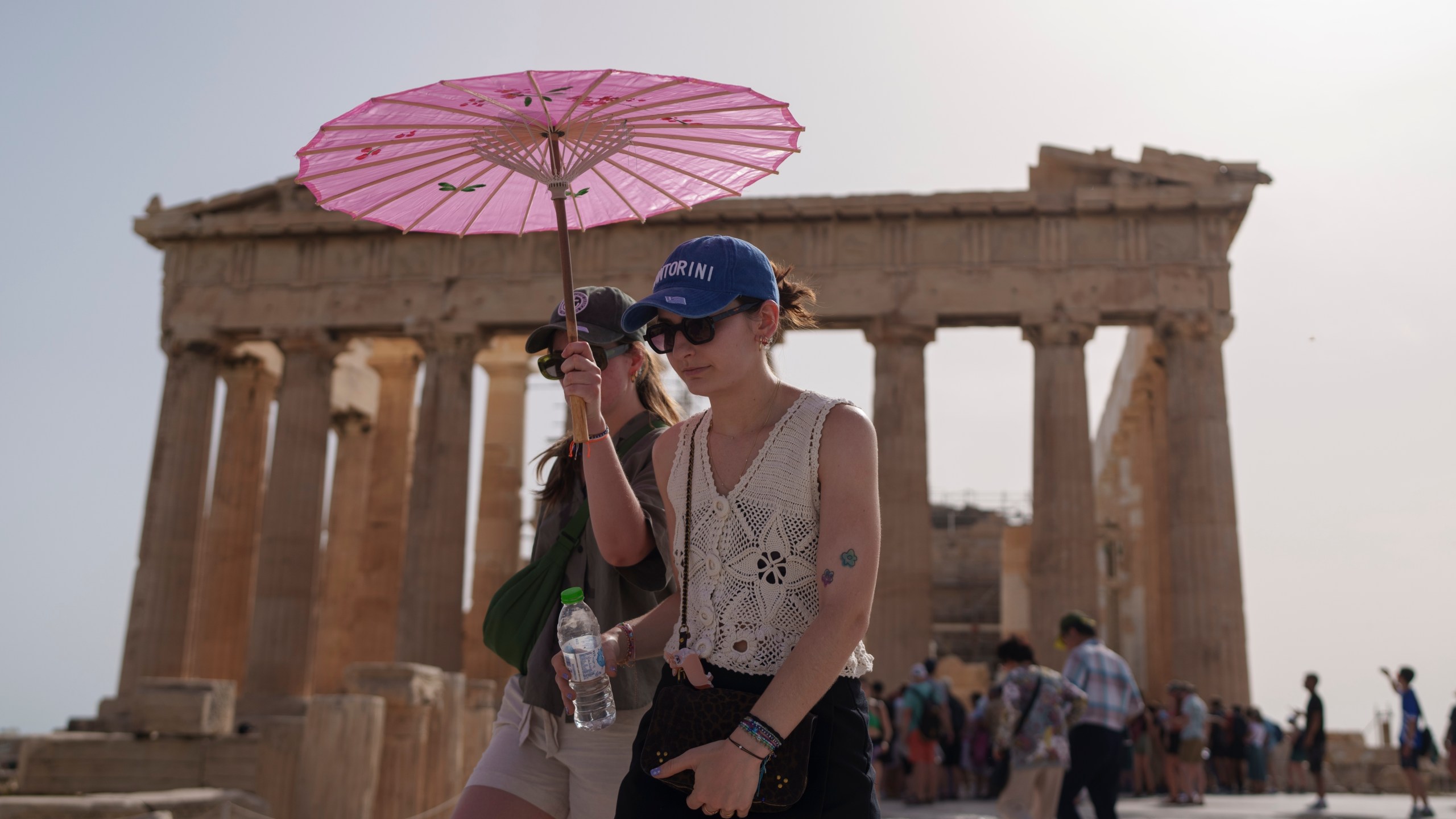 FILE - Tourists with an umbrella walk in front of the Parthenon at the ancient Acropolis in central Athens, June 12, 2024. (AP Photo/Petros Giannakouris, File)