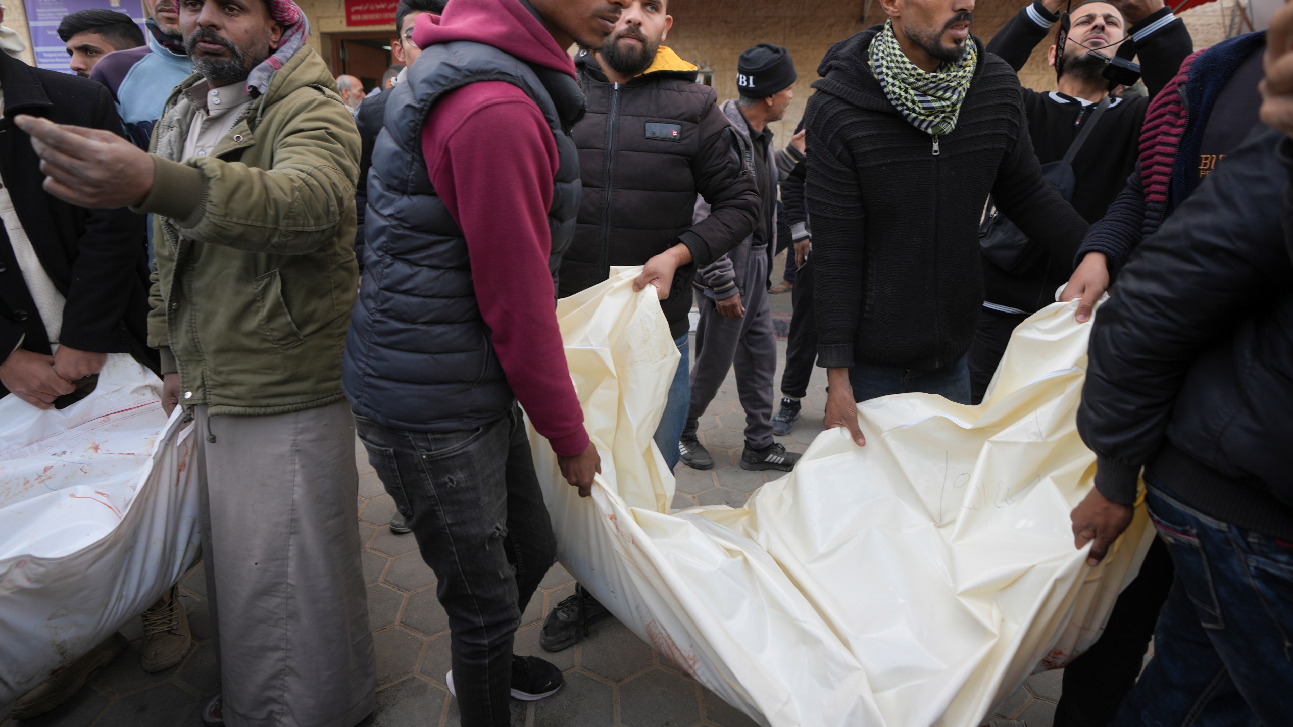 Palestinians carry white sacks containing the bodies of those killed in overnight Israeli airstrikes on the Maghazi refugee camp, at Al-Aqsa Hospital, in Deir al-Balah, central Gaza Strip, Saturday, Dec. 28, 2024. (AP Photo/Abdel Kareem Hana)