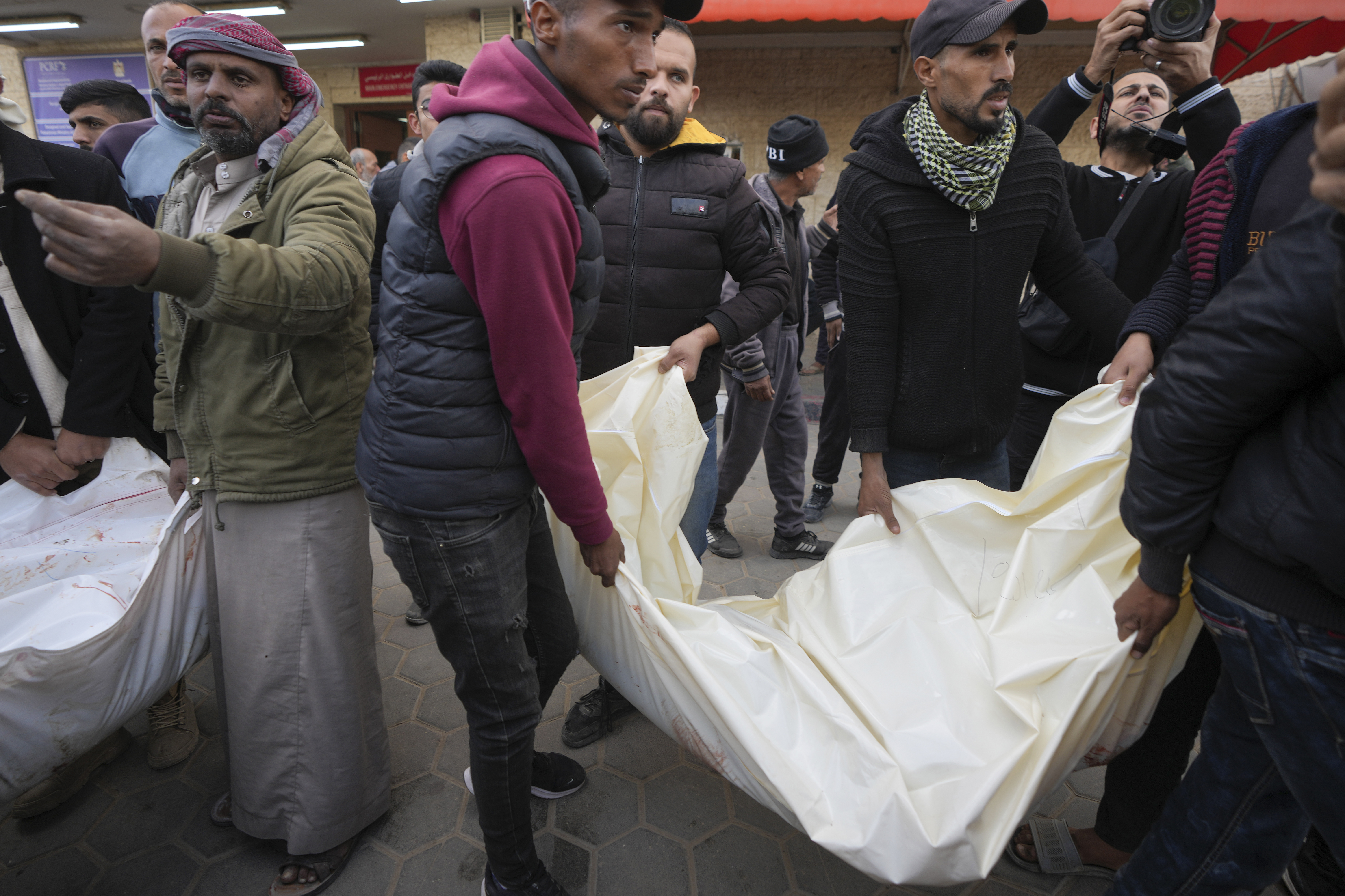 Palestinians carry white sacks containing the bodies of those killed in overnight Israeli airstrikes on the Maghazi refugee camp, at Al-Aqsa Hospital, in Deir al-Balah, central Gaza Strip, Saturday, Dec. 28, 2024. (AP Photo/Abdel Kareem Hana)