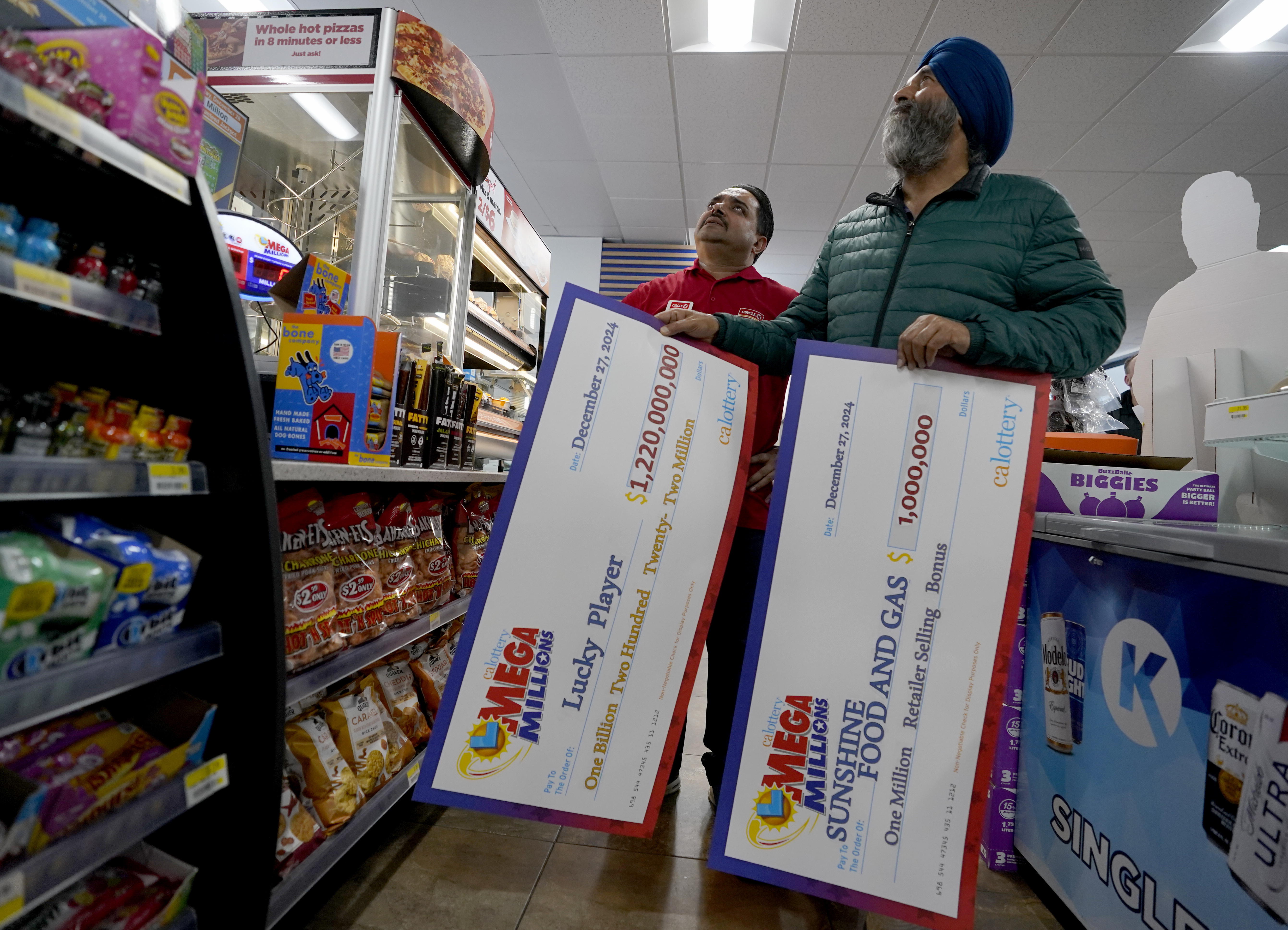 Jaspal Singh, right, and store employee Bob Singh, left, look for a spot to place two enlarged images of lottery payoff checks, at the family store, Saturday, Dec. 28, 2024, where the winning lotto ticket was purchased in Cottonwood, Calif. (AP Photo/Rich Pedroncelli).