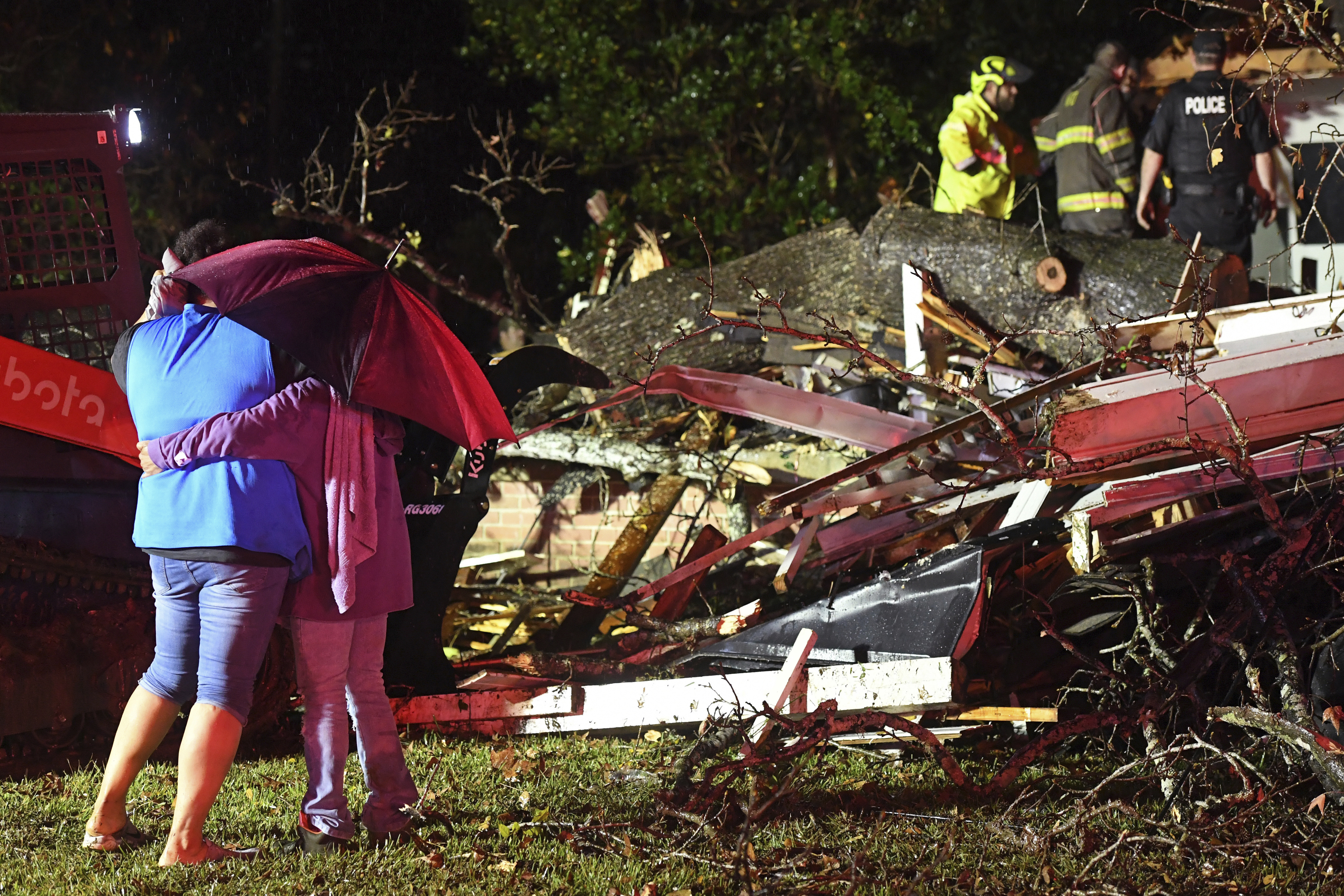 Bystanders hug as first responders work to free a victim after a tree fell on a house in Natchez, Miss., Saturday, Dec. 28, 2024. (Thomas Graning/The Natchez Democrat via AP)