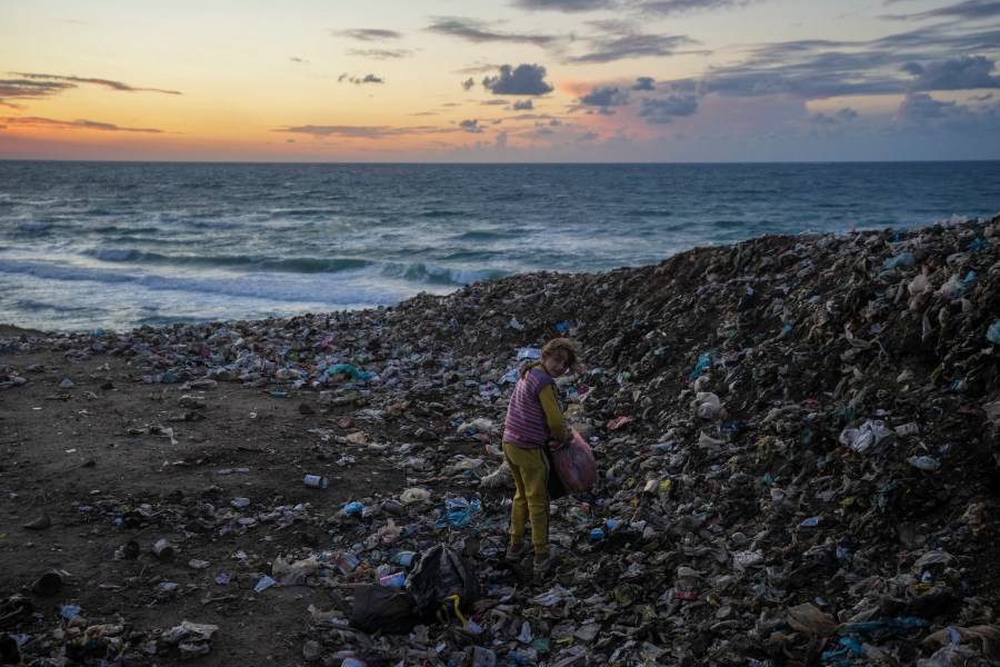 A girl searches for cardboard in the trash to make a fire, near a tent camp for displaced Palestinians by the sea in Deir al-Balah, central Gaza Strip, Monday, Dec. 30, 2024.