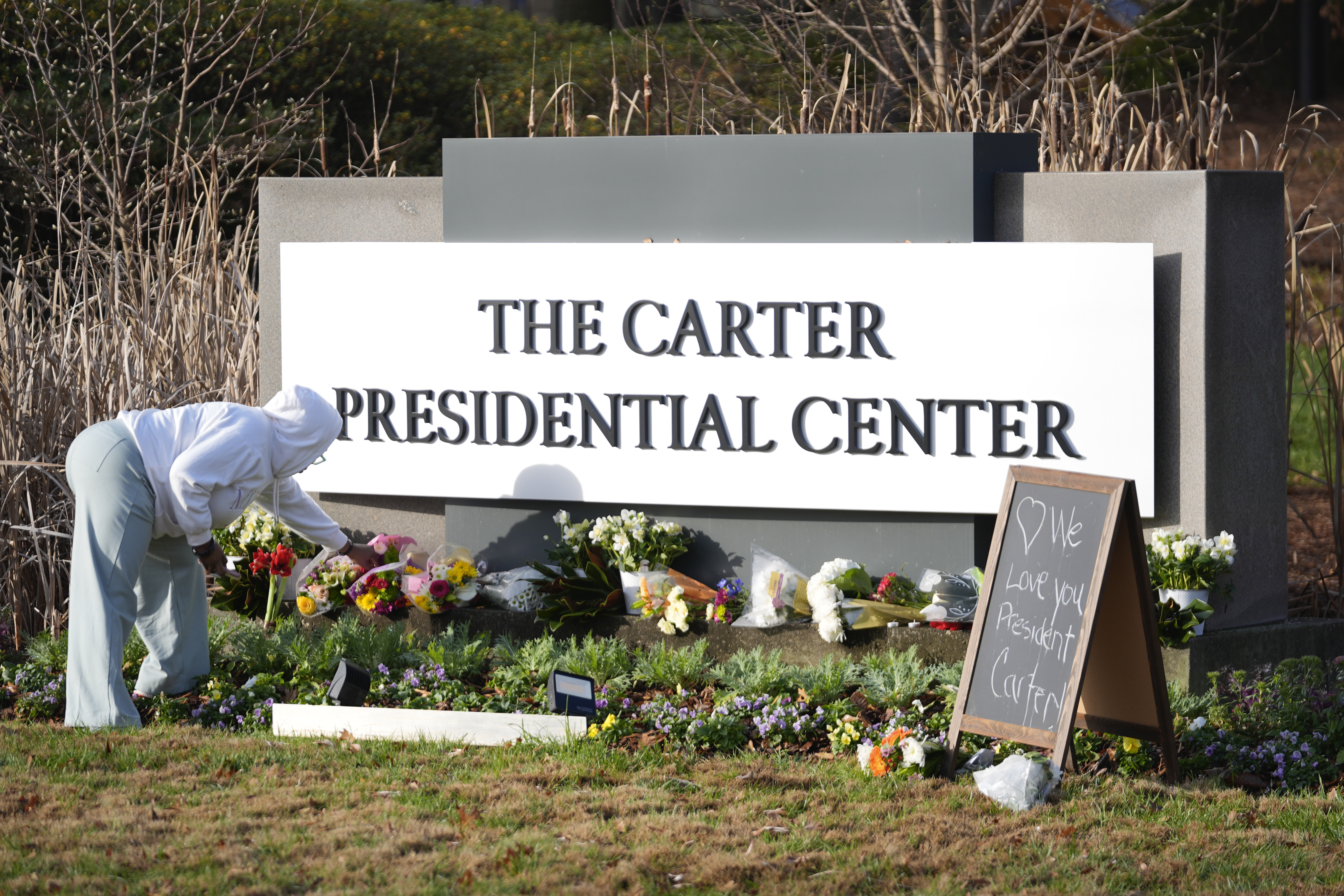 Christine Mason, of Atlanta, places flowers at entrance the The Jimmy Carter Presidential Center in Atlanta Monday, Dec. 30, 2024, in Atlanta. Formr President Jimmy Carter died Sunday at his home in Plains, Ga, at the age of 100. (AP Photo/John Bazemore )