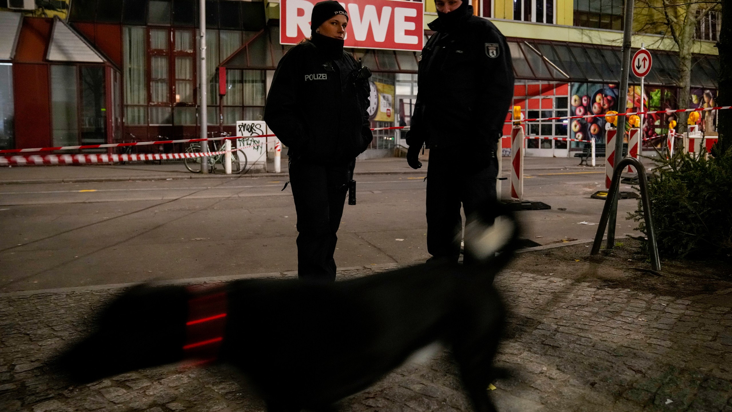 Police officers stand guard in front of a Rewe Market after a knife attack, in Berlin, Germany, Tuesday, Dec. 31, 2024. (AP Photo/Ebrahim Noroozi)