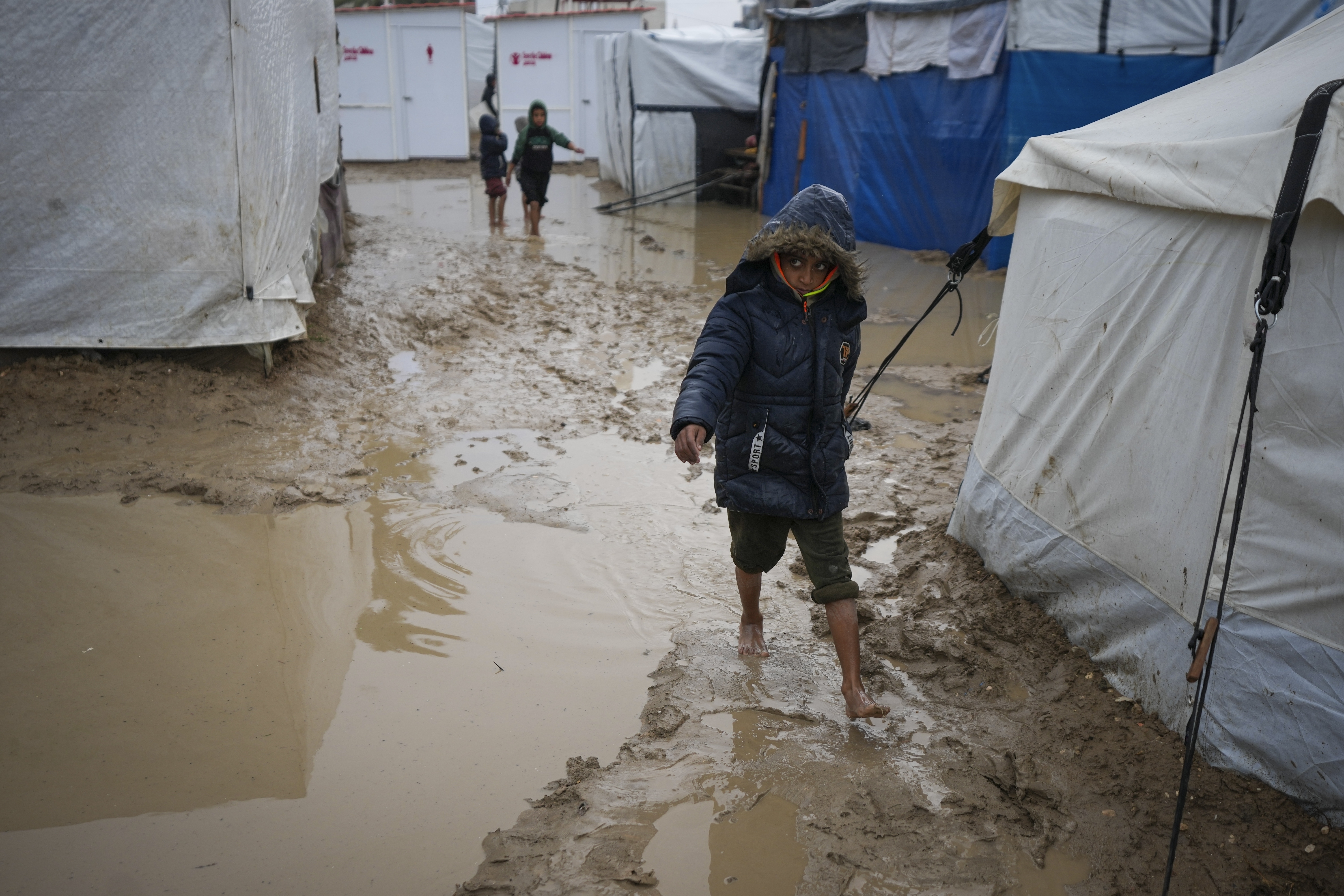 A boy walks barefoot through the mud after overnight rainfall at the refugee tent camp for displaced Palestinians in Deir al-Balah, central Gaza Strip, Tuesday, Dec. 31, 2024. (AP Photo/Abdel Kareem Hana)