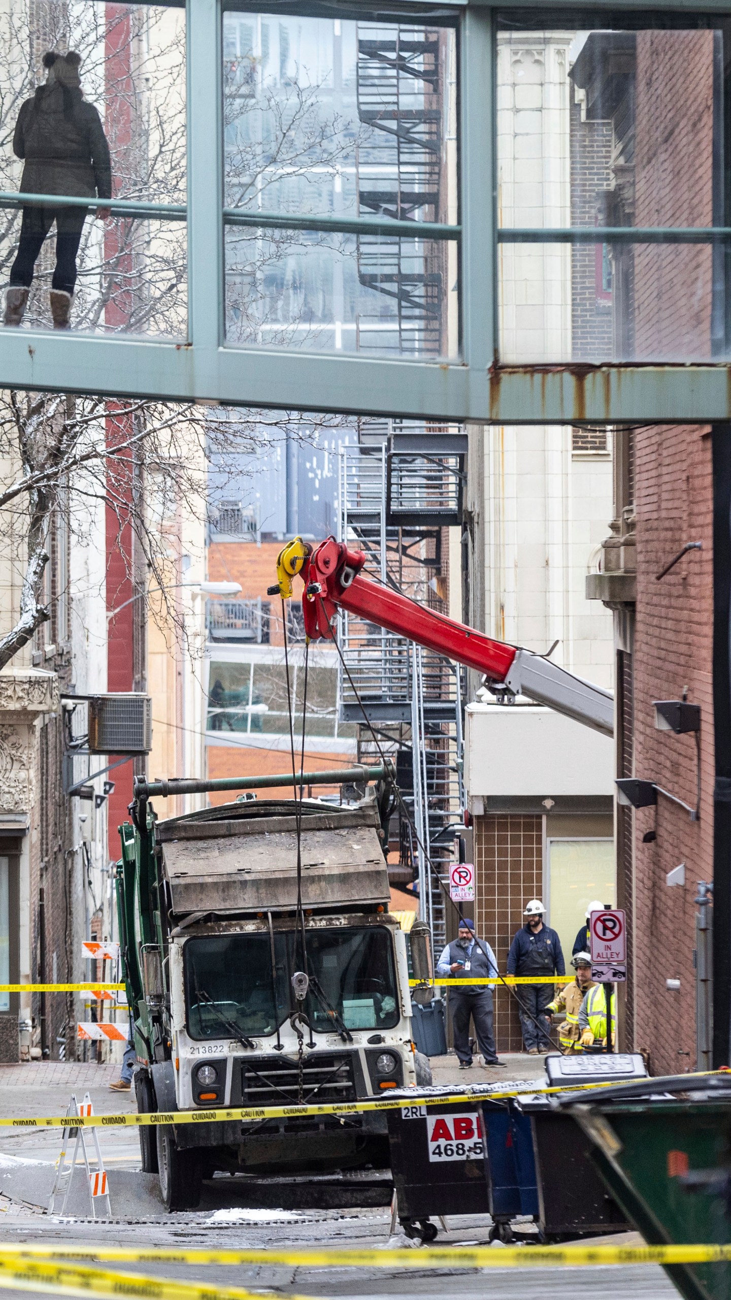 A person watches from a skywalk as workers use a crane to lift a garbage truck that got stuck in a sinkhole in downtown Omaha, Neb., Thursday, Jan. 2, 2025. (Chris Machian/Omaha World-Herald via AP)