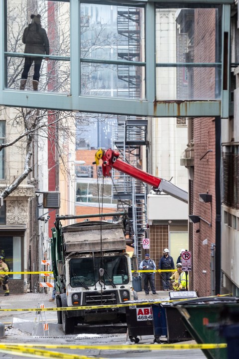 A person watches from a skywalk as workers use a crane to lift a garbage truck that got stuck in a sinkhole in downtown Omaha, Neb., Thursday, Jan. 2, 2025. (Chris Machian/Omaha World-Herald via AP)