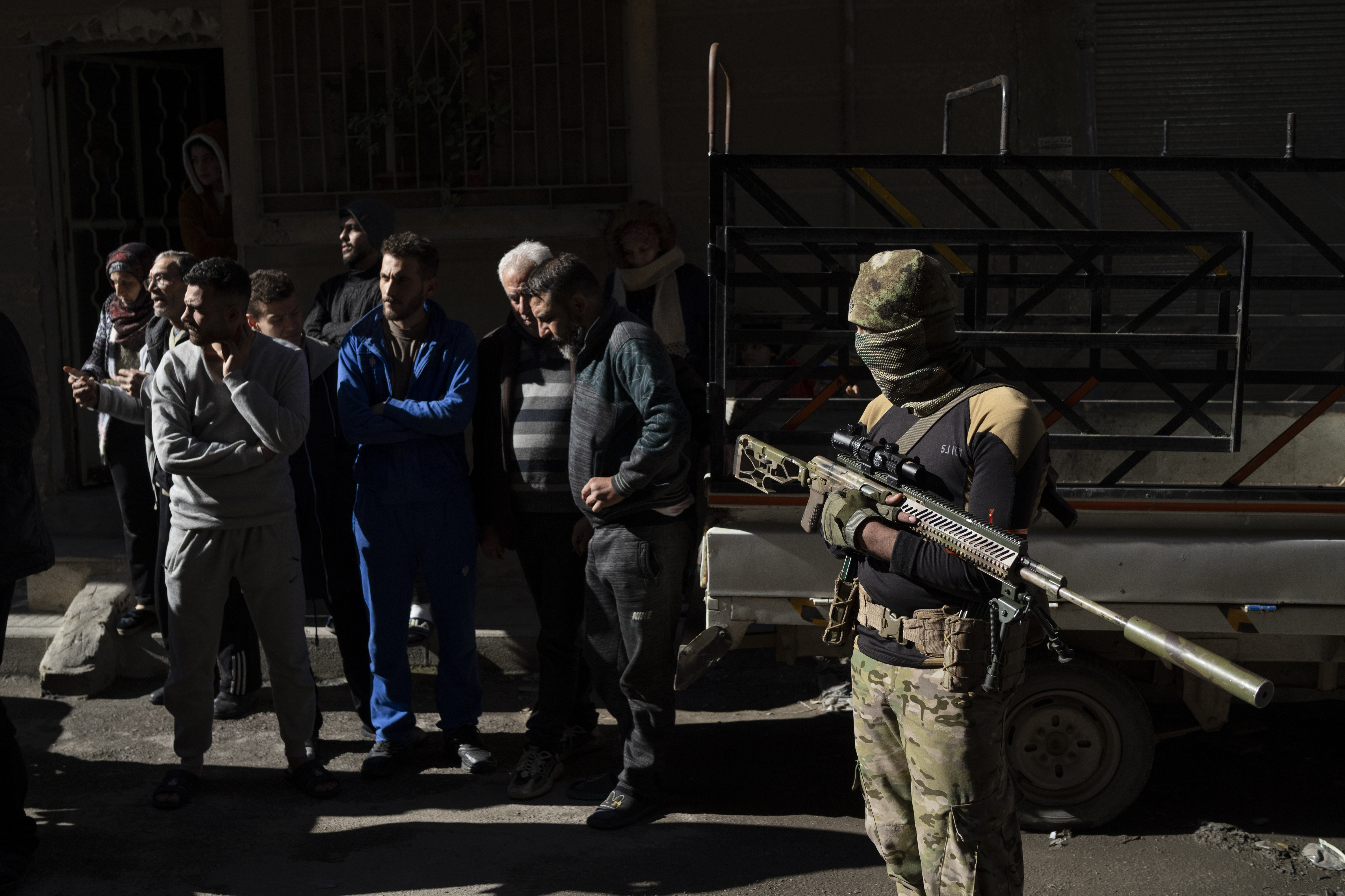 People stand outside their homes at a residential area as members of the new security forces take part in an operation to detain, according to the state media, militiamen affiliated with ousted president Bashar Assad in Homs, Syria, Thursday, Jan. 2, 2025. (AP Photo/Leo Correa)