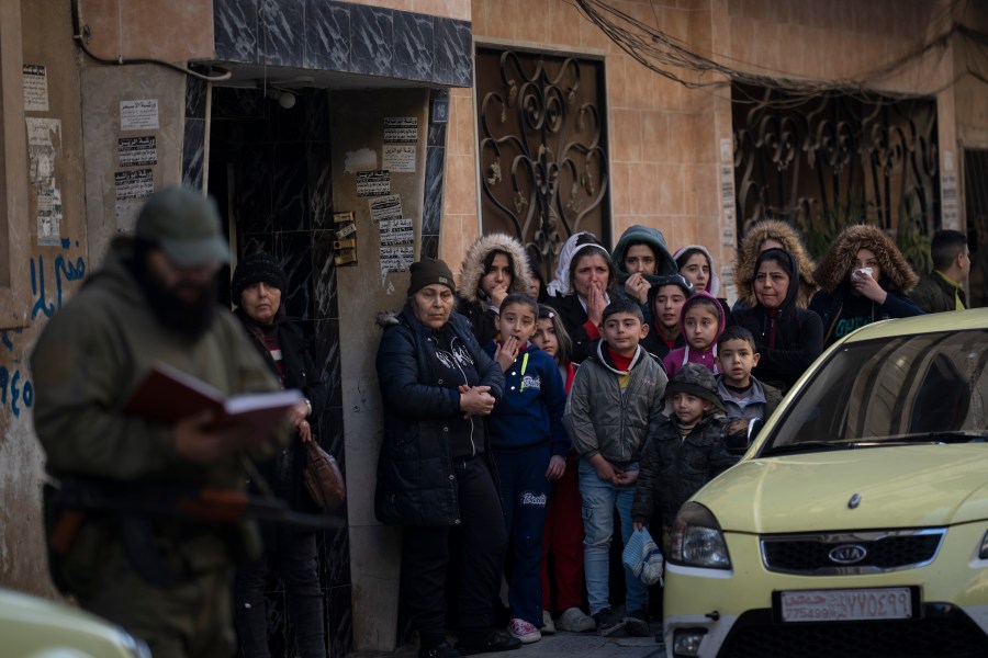 People stand outside their homes as members of the new security forces take part in an operation to detain men suspected of being part of militias or loyalist soldiers of the ousted president Bashar Assad in Homs, Syria, Friday, Jan. 3, 2025. (AP Photo/Leo Correa)