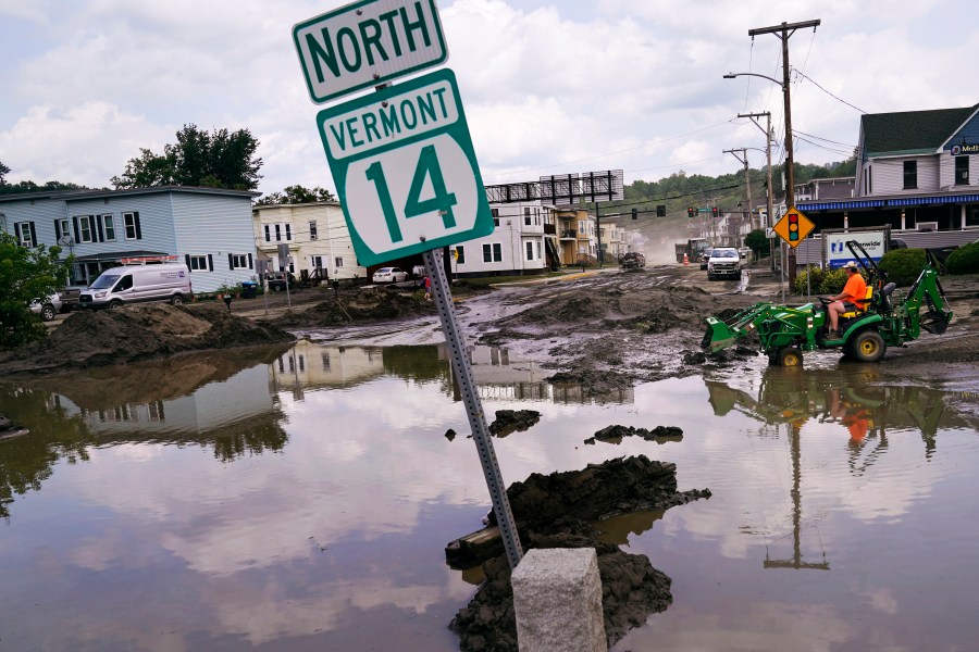 FILE - A small tractor clears water from a business as flood waters block a street, July 12, 2023, in Barre, Vt. (AP Photo/Charles Krupa, File)