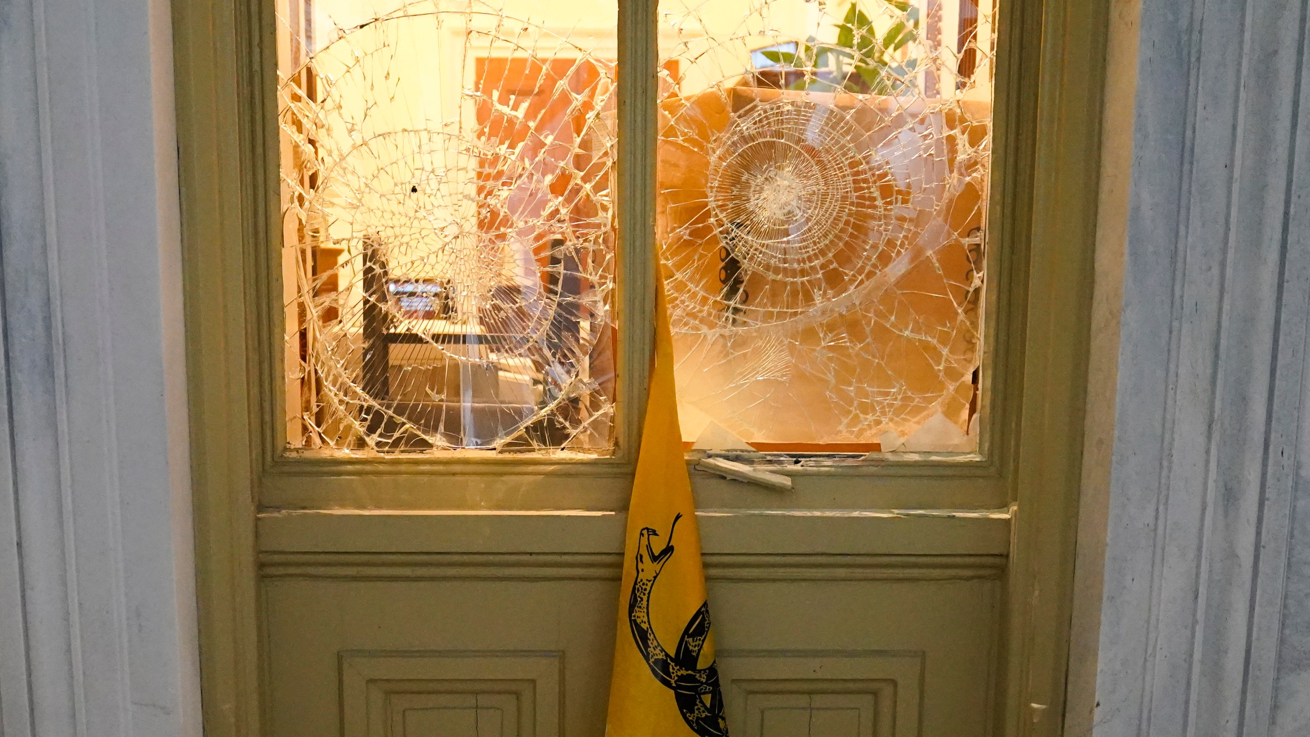 FILE - A flag hangs between broken windows after then-President Donald Trump supporters tried to break through police barriers outside the U.S. Capitol, Jan 6, 2021. (AP Photo/John Minchillo, File)