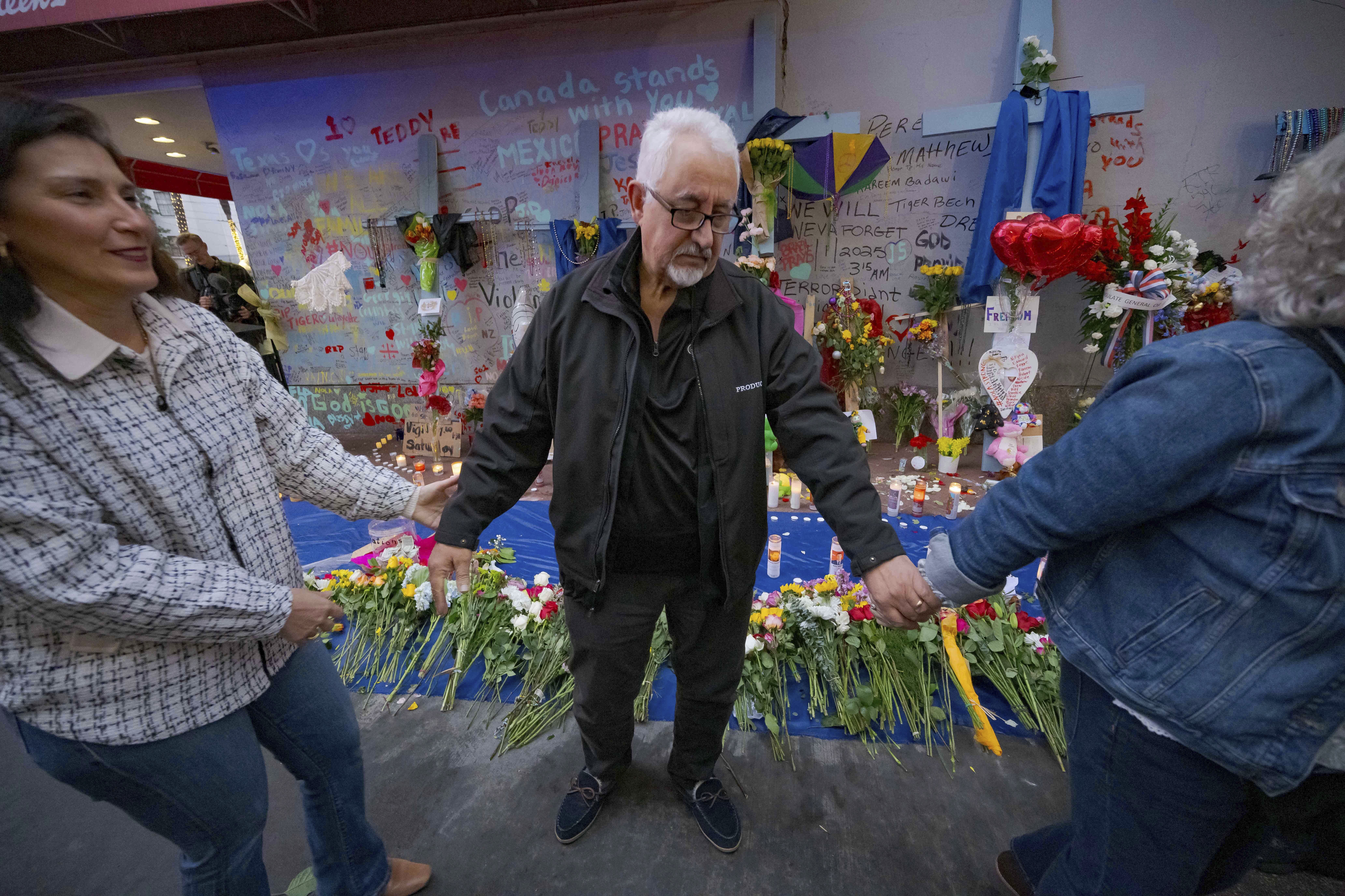 Long Island, New York residents Louis Tenedorio holds hands with family friend Angelique Whittington, left, and his wife, Cathy Tenedorio, by a memorial on Bourbon Street and Canal Street in New Orleans, Saturday, Jan. 4, 2025, where his son, Matthew Tenedorio, was killed as one of the victims of the New Year's Day deadly truck attack and shooting. (AP Photo/Matthew Hinton)