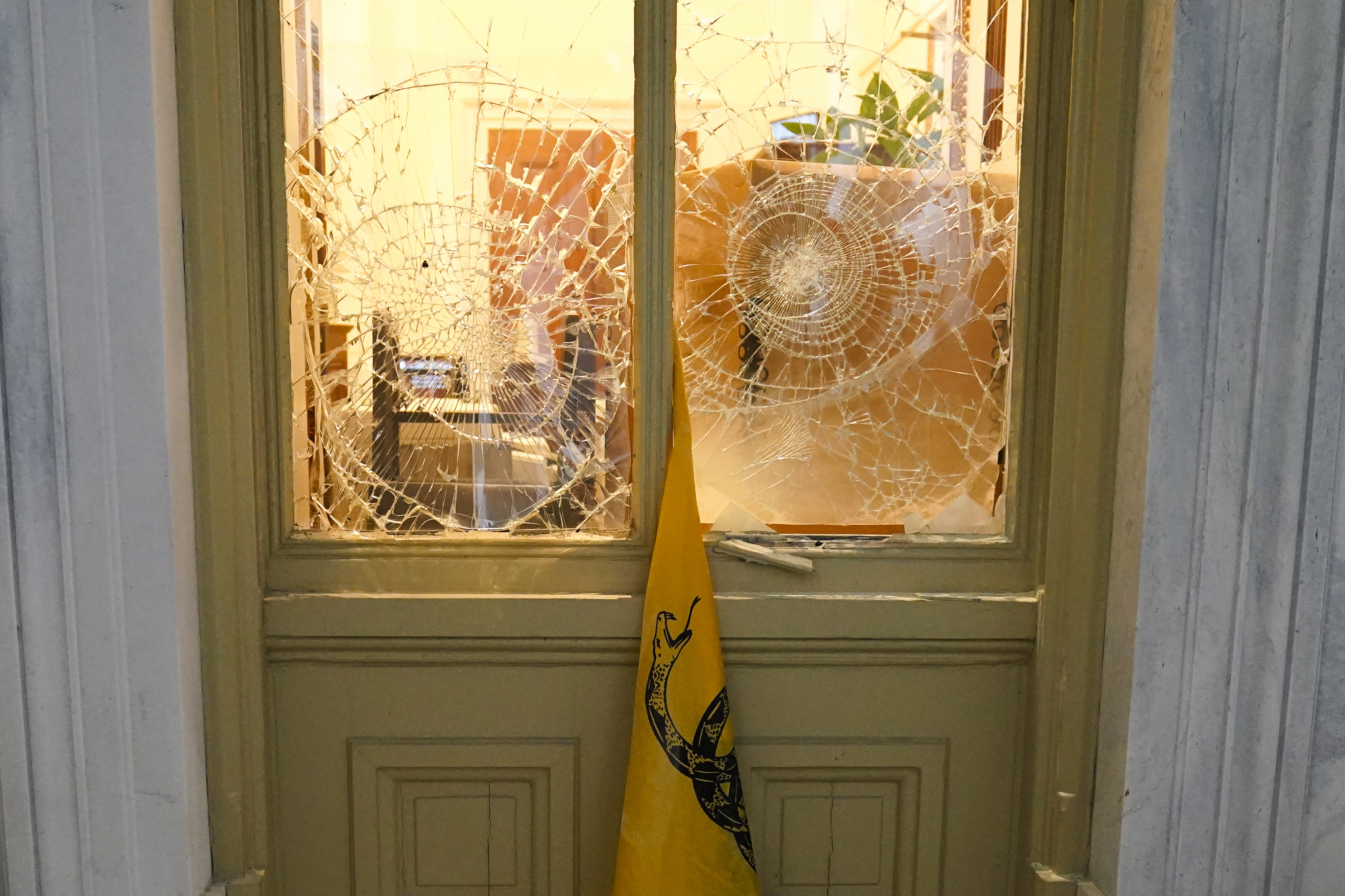 FILE - A flag hangs between broken windows after then-President Donald Trump supporters tried to break through police barriers outside the U.S. Capitol, Jan 6, 2021. (AP Photo/John Minchillo, File)