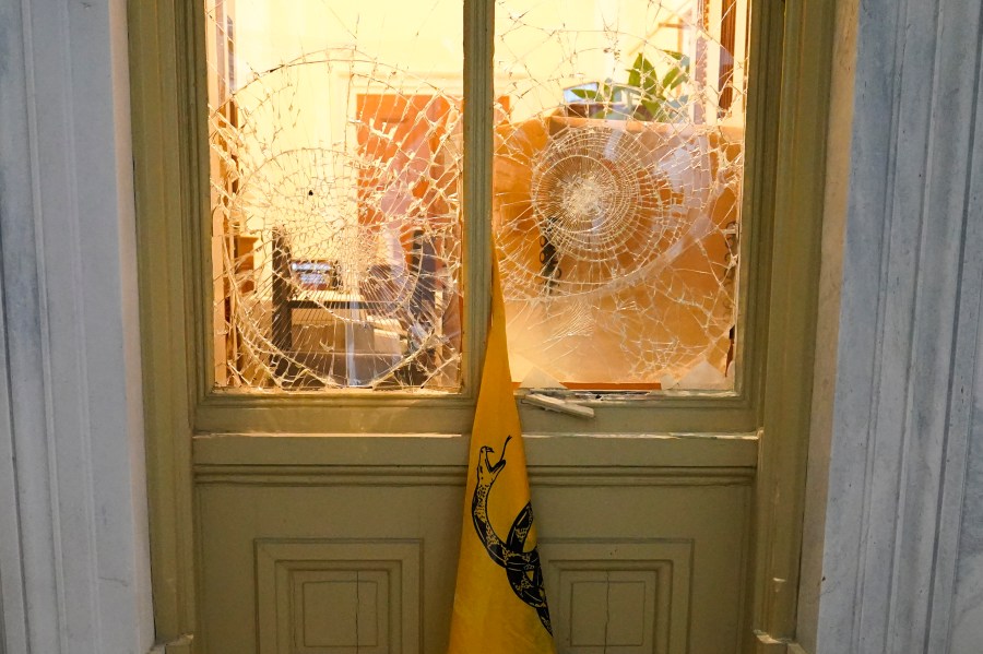 FILE - A flag hangs between broken windows after then-President Donald Trump supporters tried to break through police barriers outside the U.S. Capitol, Jan 6, 2021. (AP Photo/John Minchillo, File)