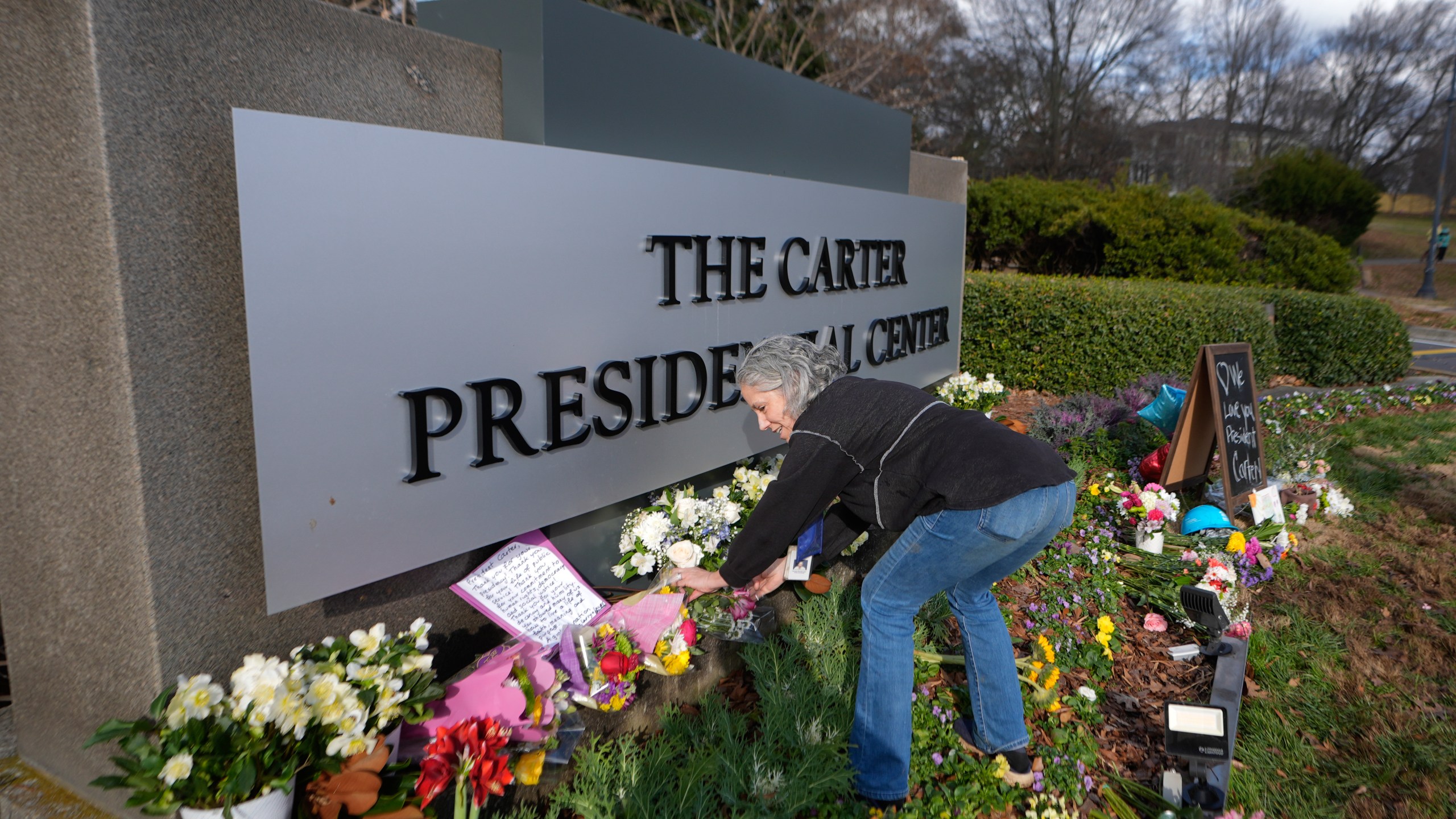 Carter Center volunteer Denise Bomberger places flowers at the entrance to the Jimmy Carter Presidential Center Tuesday, Dec. 31, 2024, in Atlanta. Carter died Sunday at he age of 100. (AP Photo/John Bazemore )