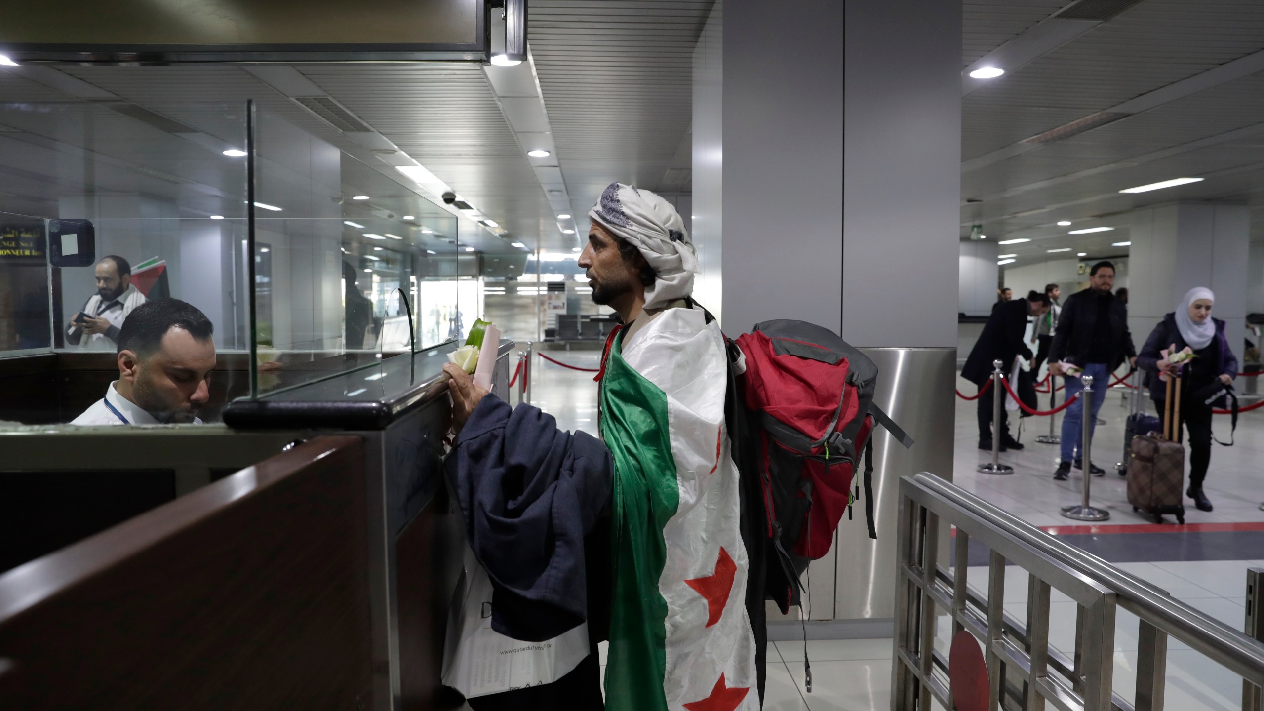 A man who arrived at a first international commercial flight since the fall of former Syrian President Bashar Assad, covers himself with the Syrian "Revolutionary" flag as he checks in at the arrival terminal of Damascus international airport, in Damascus, Syria, Tuesday, Jan. 7, 2025. (AP Photo/Omar Sanadiki)