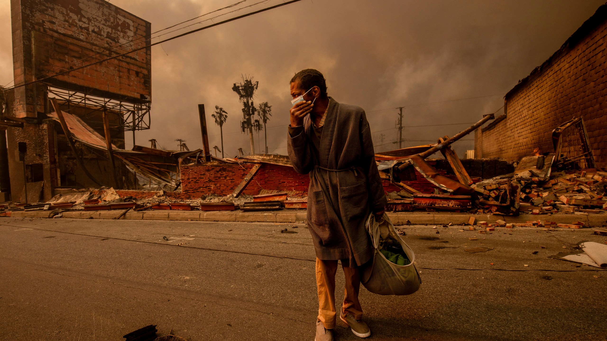 A man walks past a fire-ravaged business after the Eaton Fire swept through Wednesday, Jan. 8, 2025, in Altadena, Calif. (AP Photo/Ethan Swope)