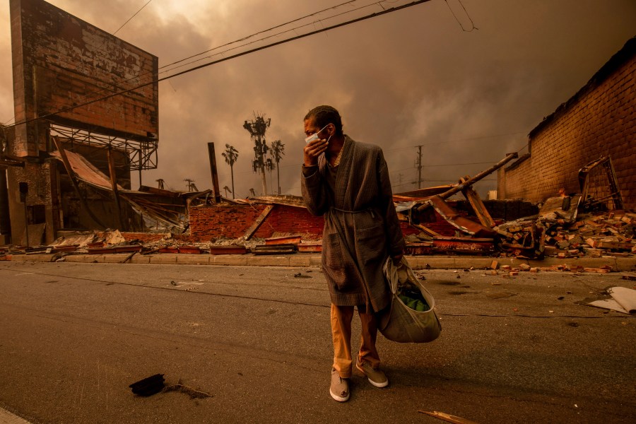 A man walks past a fire-ravaged business after the Eaton Fire swept through Wednesday, Jan. 8, 2025, in Altadena, Calif. (AP Photo/Ethan Swope)