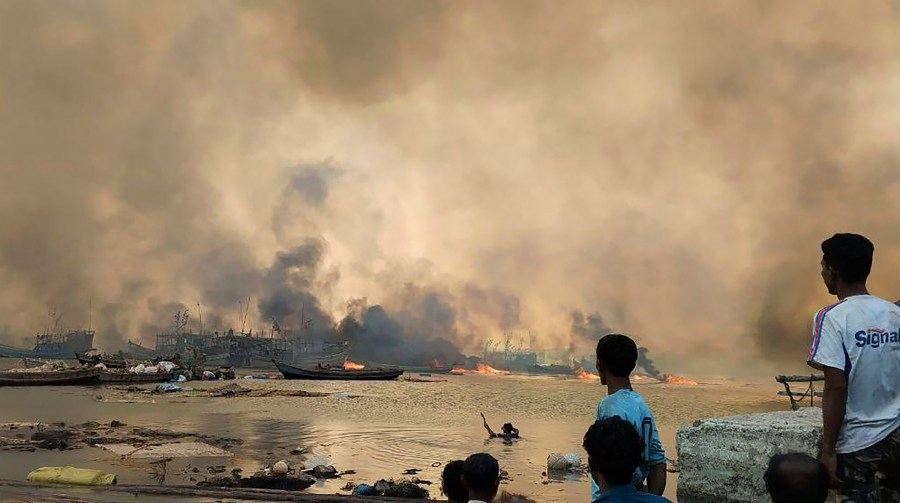 This handout photo provided by the Arakan Army shows people looking at flames rising after an airstrike by the ruling military in Kyauk Ni Maw village, in Ramree township, also pronounced Yanbye, in Rakhine state, Myanmar, Wednesday, Jan.8, 2025. (The Arakan Army via AP)