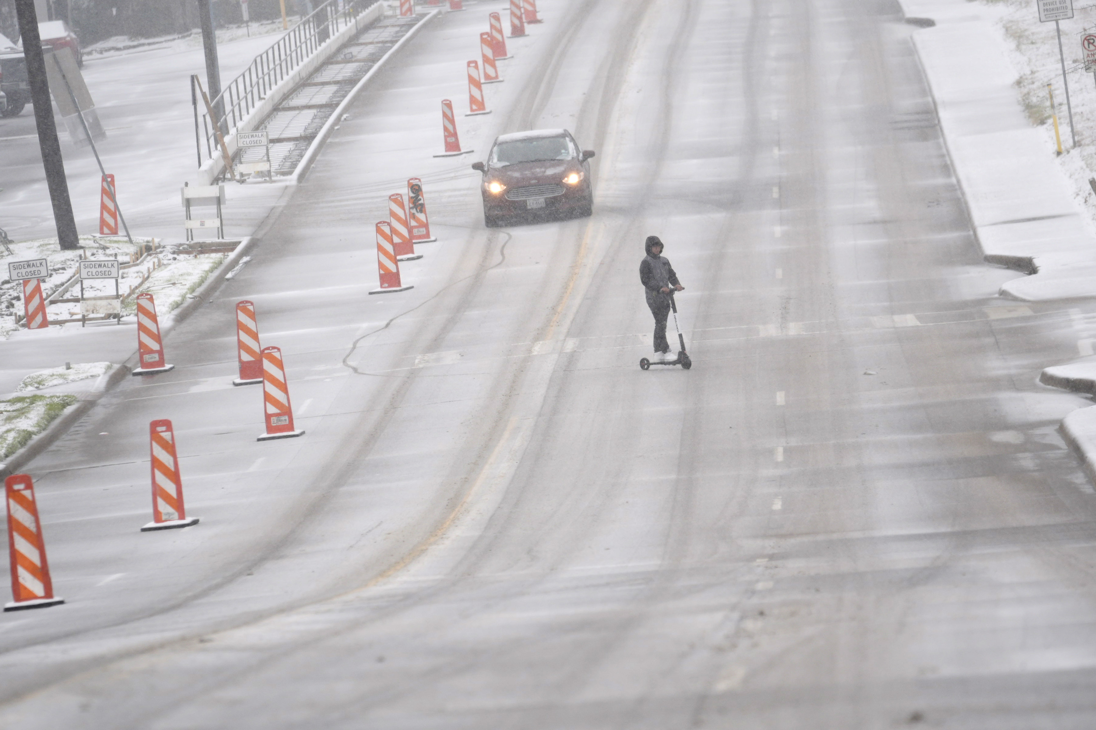 Snow falls as a car and a scooter make their way along a street Thursday, Jan. 9, 2025, in Dallas. (AP Photo/LM Otero)