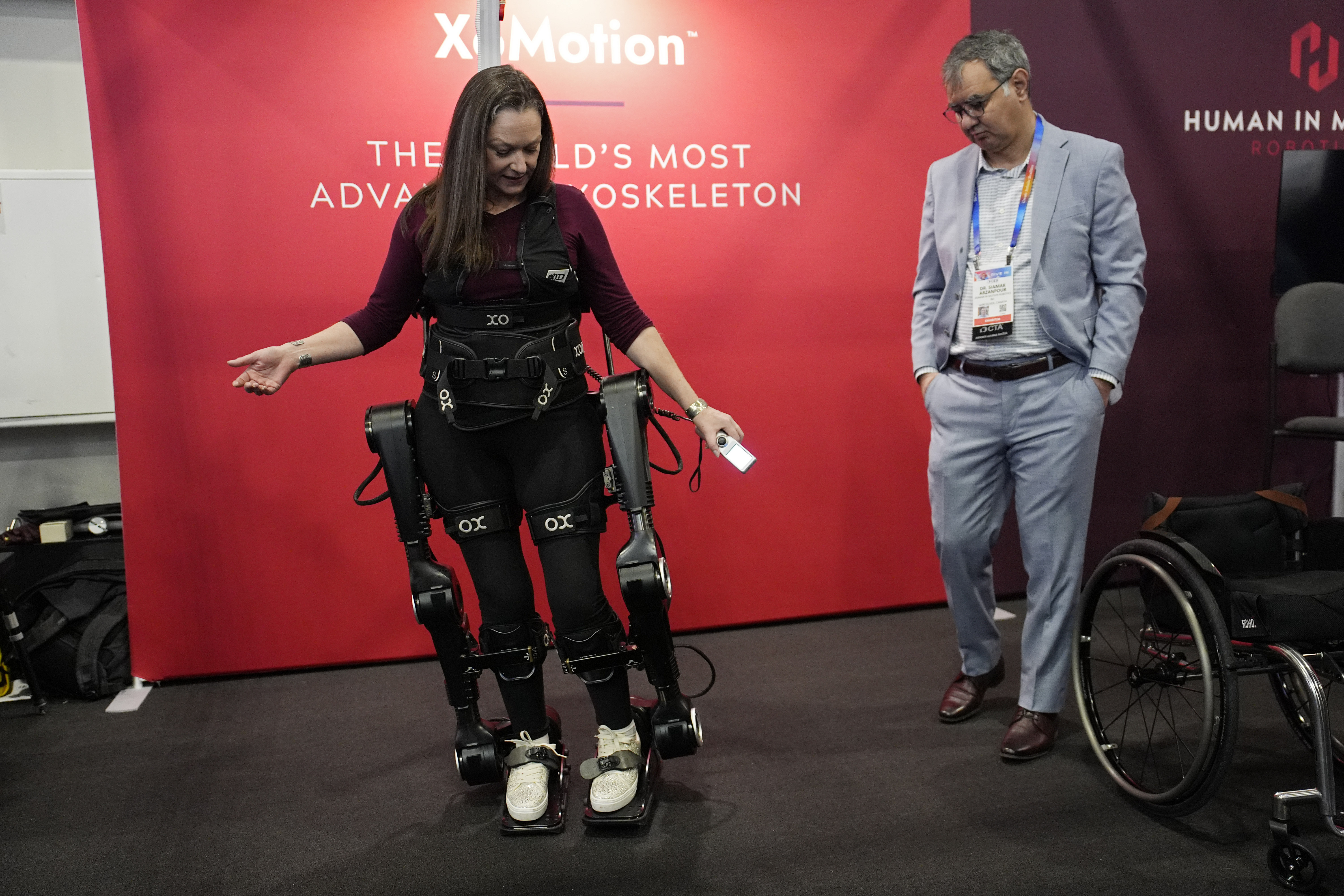 Chloe Angus, director of Lived Experience at Human in Motion Robotics and paraplegic, stands and moves with help from the XoMotion exoskeleton at the Human In Motion Robotics booth during the CES tech show Wednesday, Jan. 8, 2025, in Las Vegas. The wearable robotic exoskeleton is designed to assist patients with mobility impairments due to spinal cord injuries, stroke and other neurological conditions in standing up and walking. (AP Photo/John Locher)