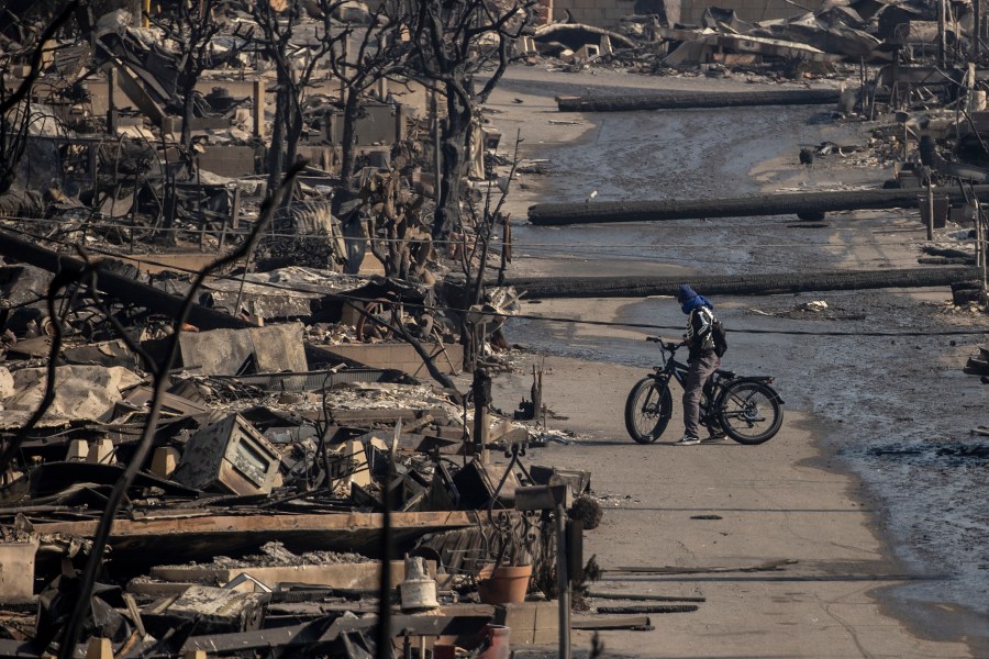 A bicyclist stands amongst Pacific Palisades Bowl Mobile Estates destroyed by the Palisades Fire in Pacific Palisades, Calif., Thursday, Jan. 9, 2025.(Stephen Lam/San Francisco Chronicle via AP)