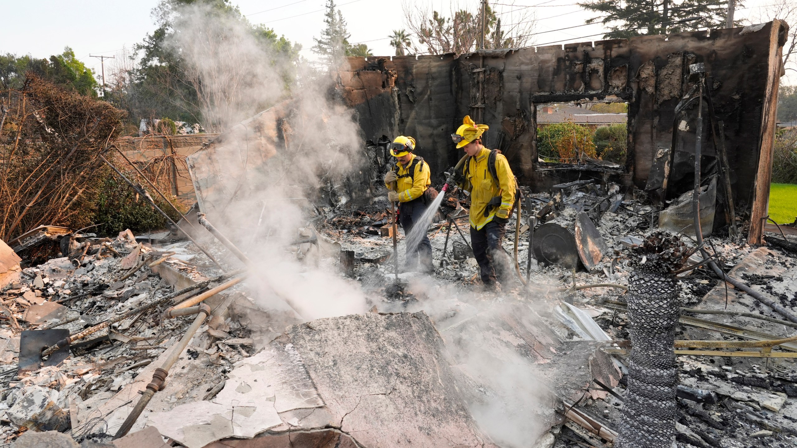 Firefighters extinguish burning embers at a house on Santa Rosa Avenue, also known as Christmas Tree Lane, after the house was destroyed by the Eaton Fire, Thursday, Jan. 9, 2025, in Altadena, Calif. (AP Photo/Chris Pizzello)