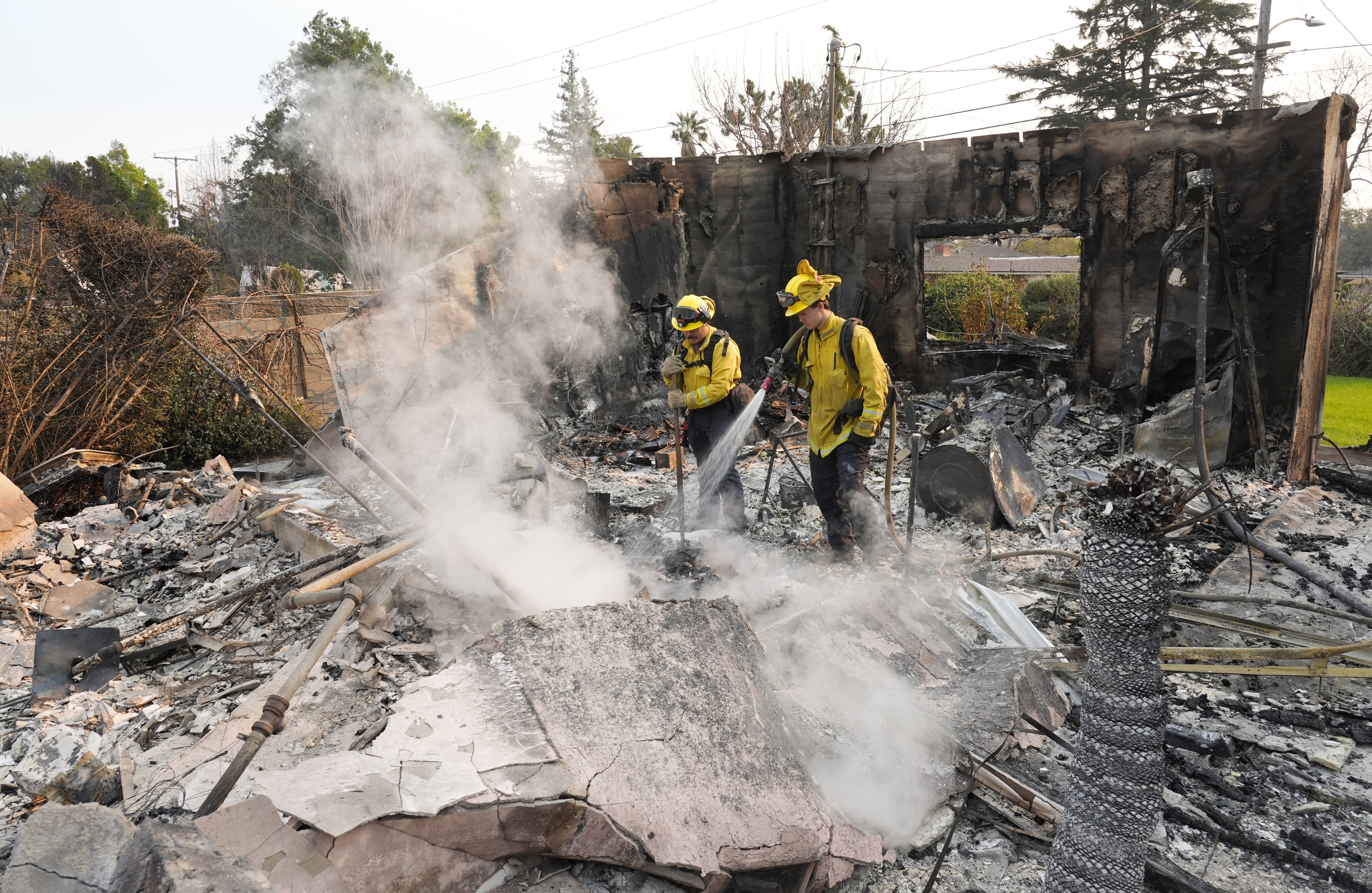 Firefighters extinguish burning embers at a house on Santa Rosa Avenue, also known as Christmas Tree Lane, after the house was destroyed by the Eaton Fire, Thursday, Jan. 9, 2025, in Altadena, Calif. (AP Photo/Chris Pizzello)