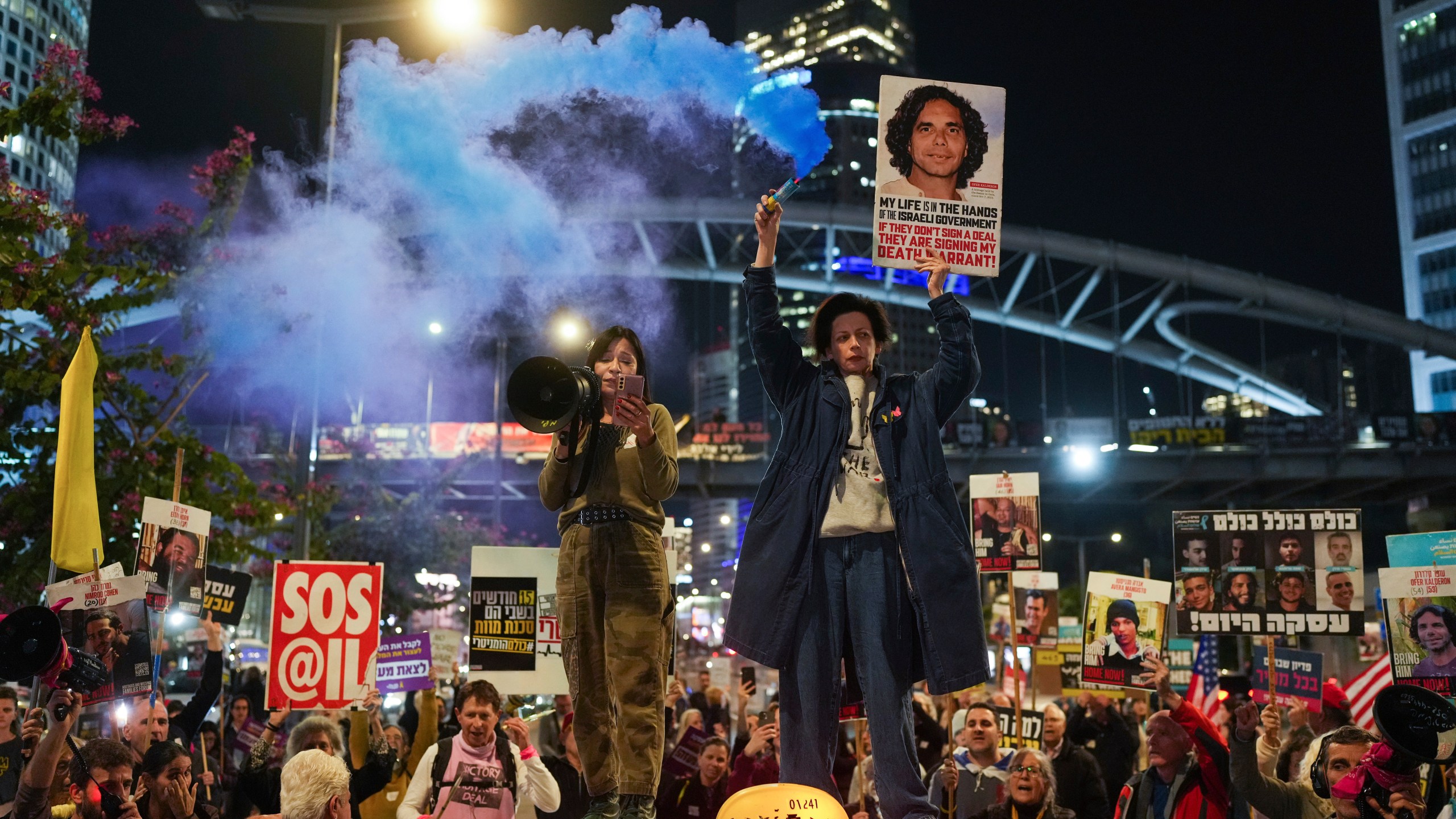 Demonstrators hold signs and flares during a protest calling for the immediate release of the hostages held in the Gaza Strip by the Hamas militant group in Tel Aviv, Israel, on Monday, Jan. 13, 2025. (AP Photo/Ohad Zwigenberg)