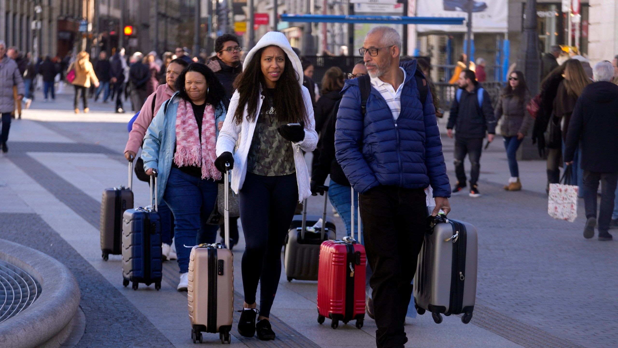 Tourists walk with suitcases in an area with short-term rentals on platforms, like AirBnB in Madrid, Spain, Tuesday, Jan. 14, 2025. (AP Photo/Paul White)