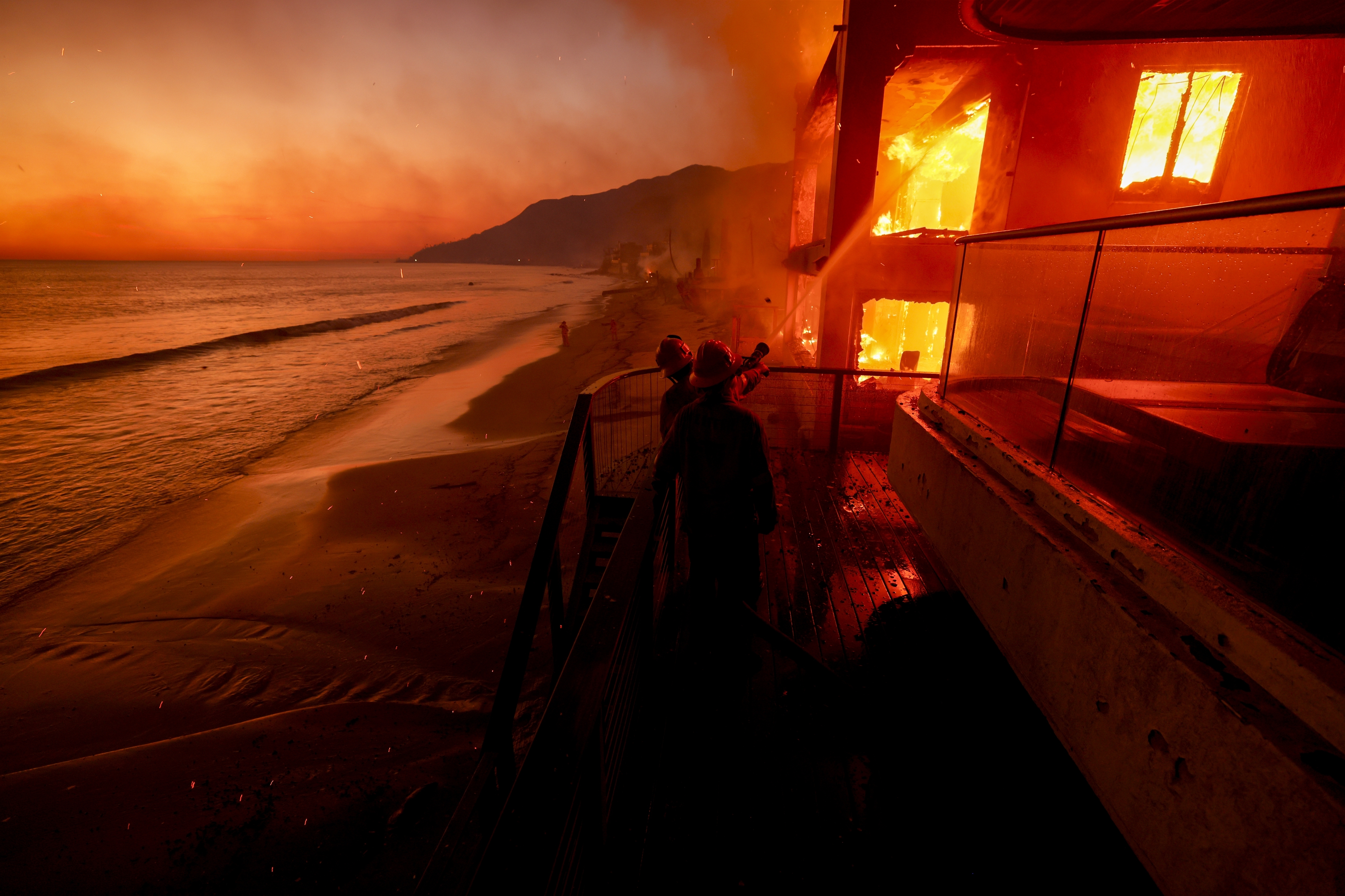 Firefighters work from a deck as the Palisades Fire burns a beachfront property Jan. 8, 2025, in Malibu, Calif. (AP Photo/Etienne Laurent)