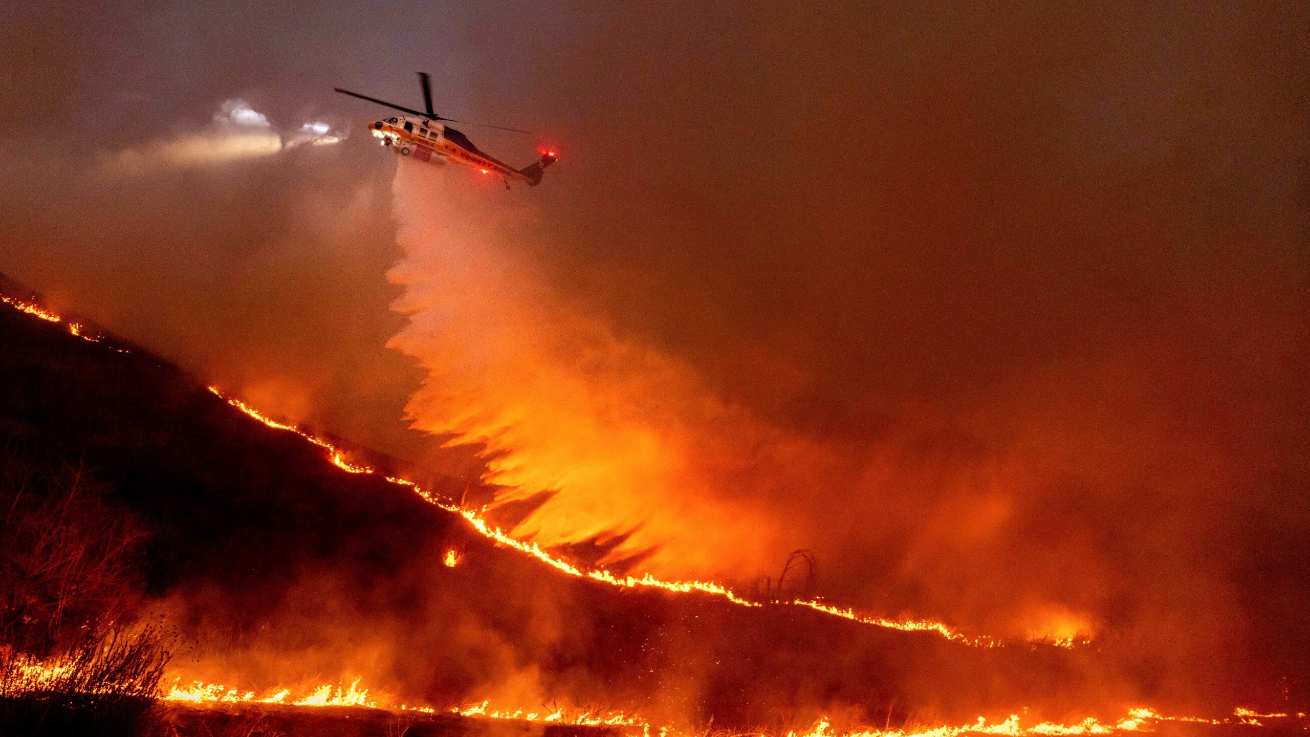 FILE - Water is dropped by helicopter on the Kenneth Fire in the West Hills section of Los Angeles, Jan. 9, 2025. (AP Photo/Ethan Swope, File)