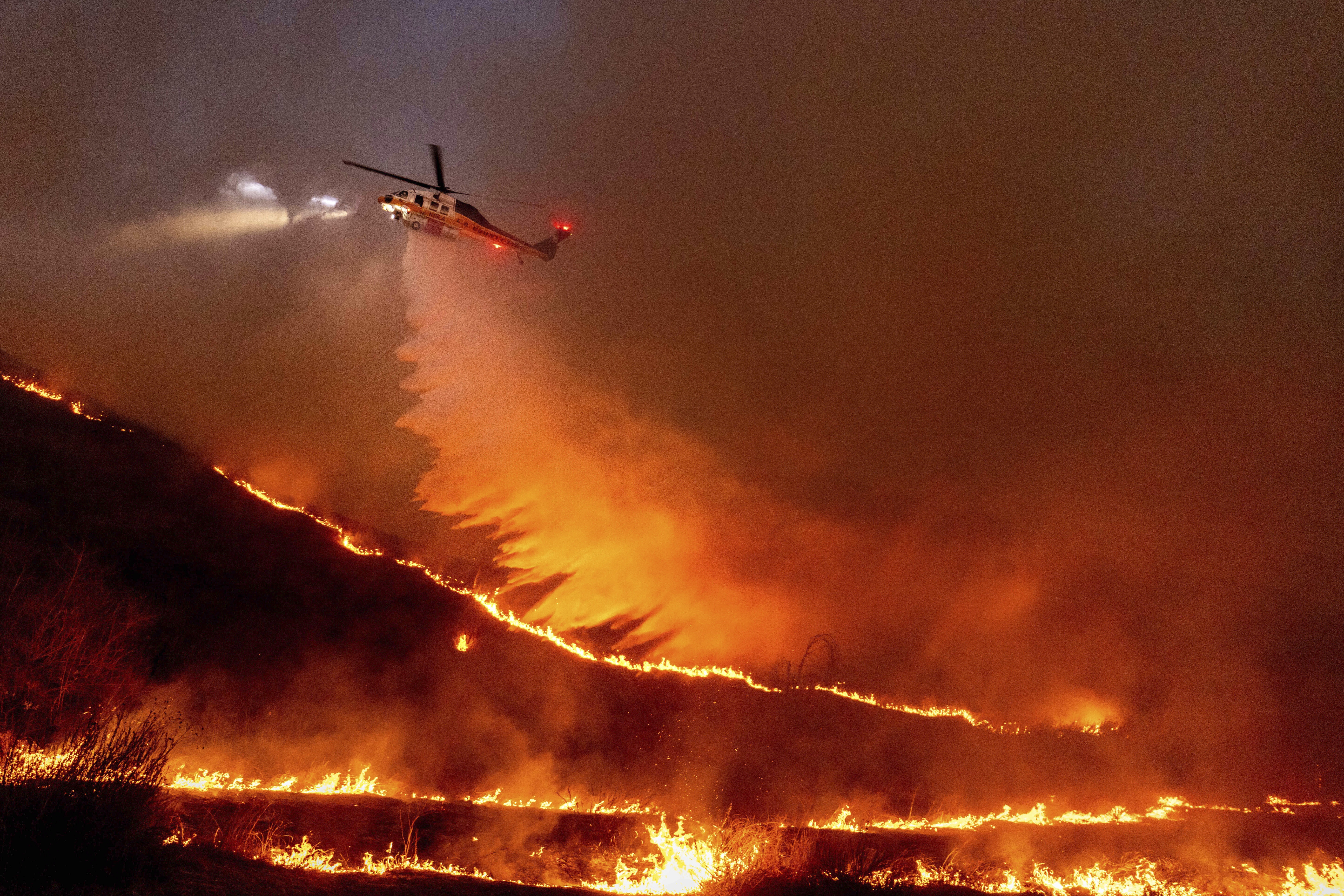 FILE - Water is dropped by helicopter on the Kenneth Fire in the West Hills section of Los Angeles, Jan. 9, 2025. (AP Photo/Ethan Swope, File)