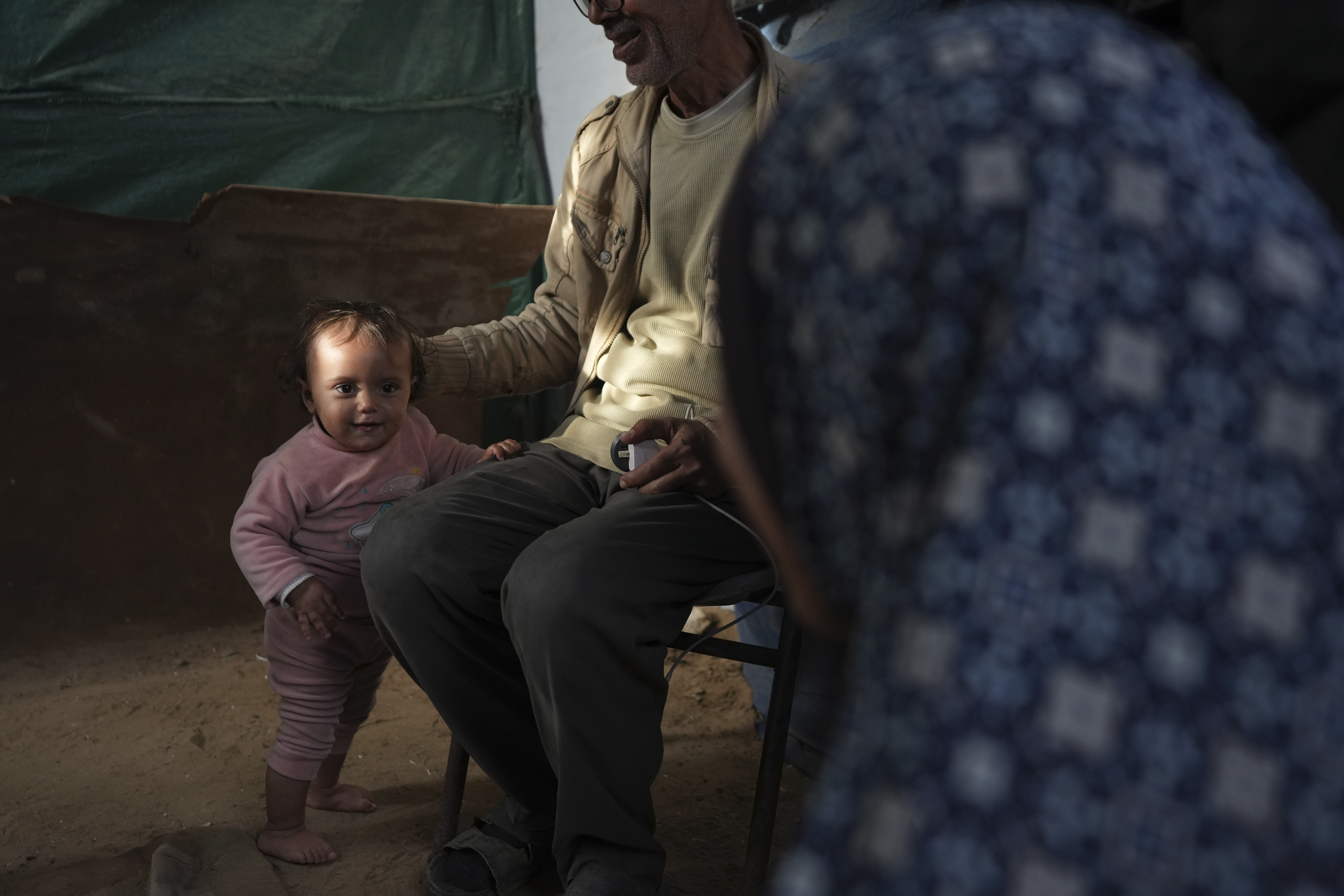 Massa Zaqout, who was born on the first day of the war in Gaza, stands next to her father in the family tent in Deir al-Balah, Gaza Strip, Tuesday, Jan. 14, 2025. (AP Photo/Abdel Kareem Hana)