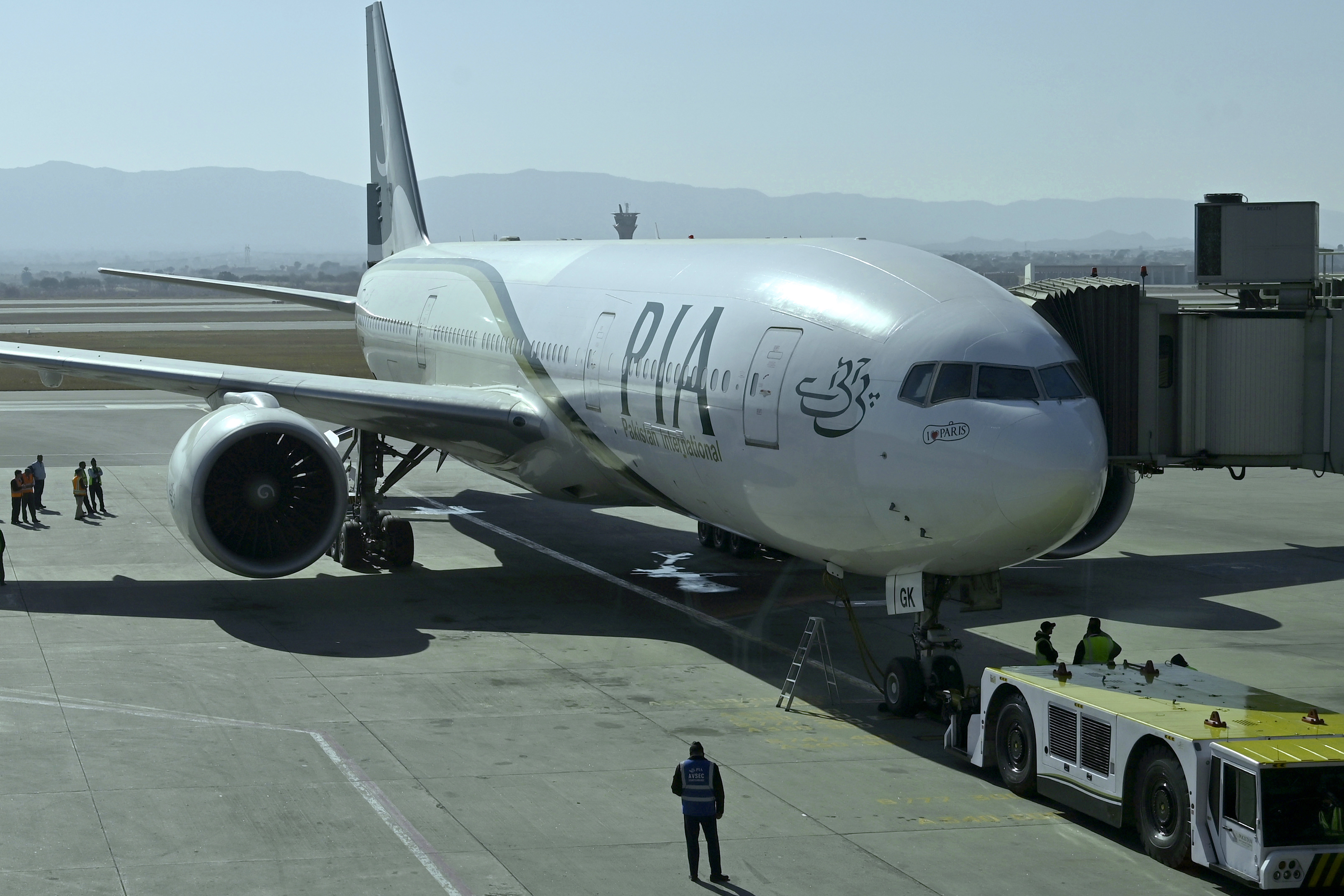 Ground staff work beside the state-run Pakistan International Airlines plane preparing to take-off for Paris after the airline resumes direct flights to Europe after EU lifted a four-year ban, at the Islamabad International Airport, in Islamabad, Pakistan, Friday, Jan. 10, 2025. (AP Photo)