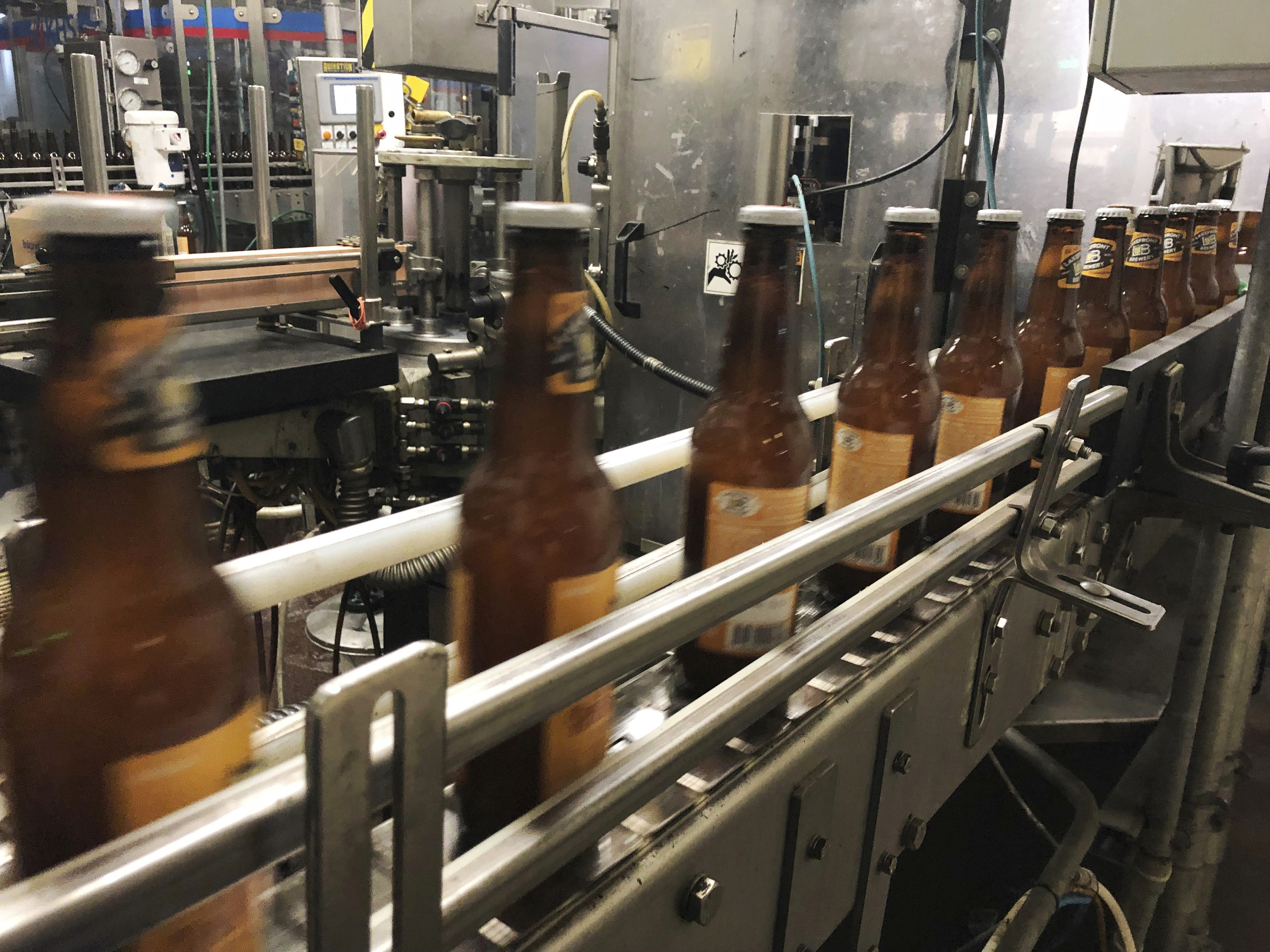 FILE- Bottles freshly filled with beer move on a conveyor belt at Lakefront Brewery in Milwaukee, Jan. 14, 2019. (AP Photo/Carrie Antlfinger, File)