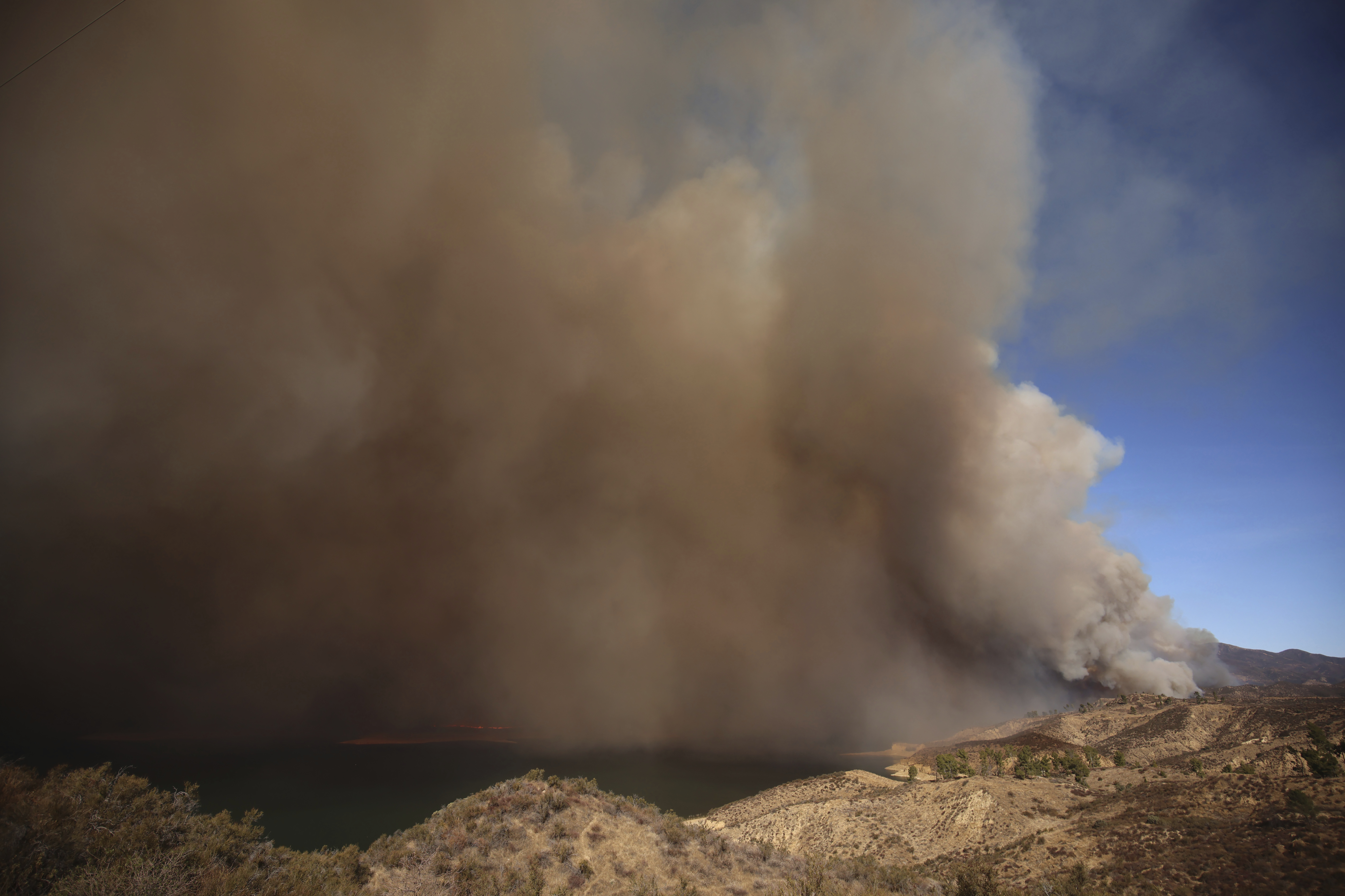 Plumes of smoke caused by the Hughes Fire rise over Lake Castaic, Calif., Wednesday, Jan. 22, 2025. (AP Photo/Ethan Swope)