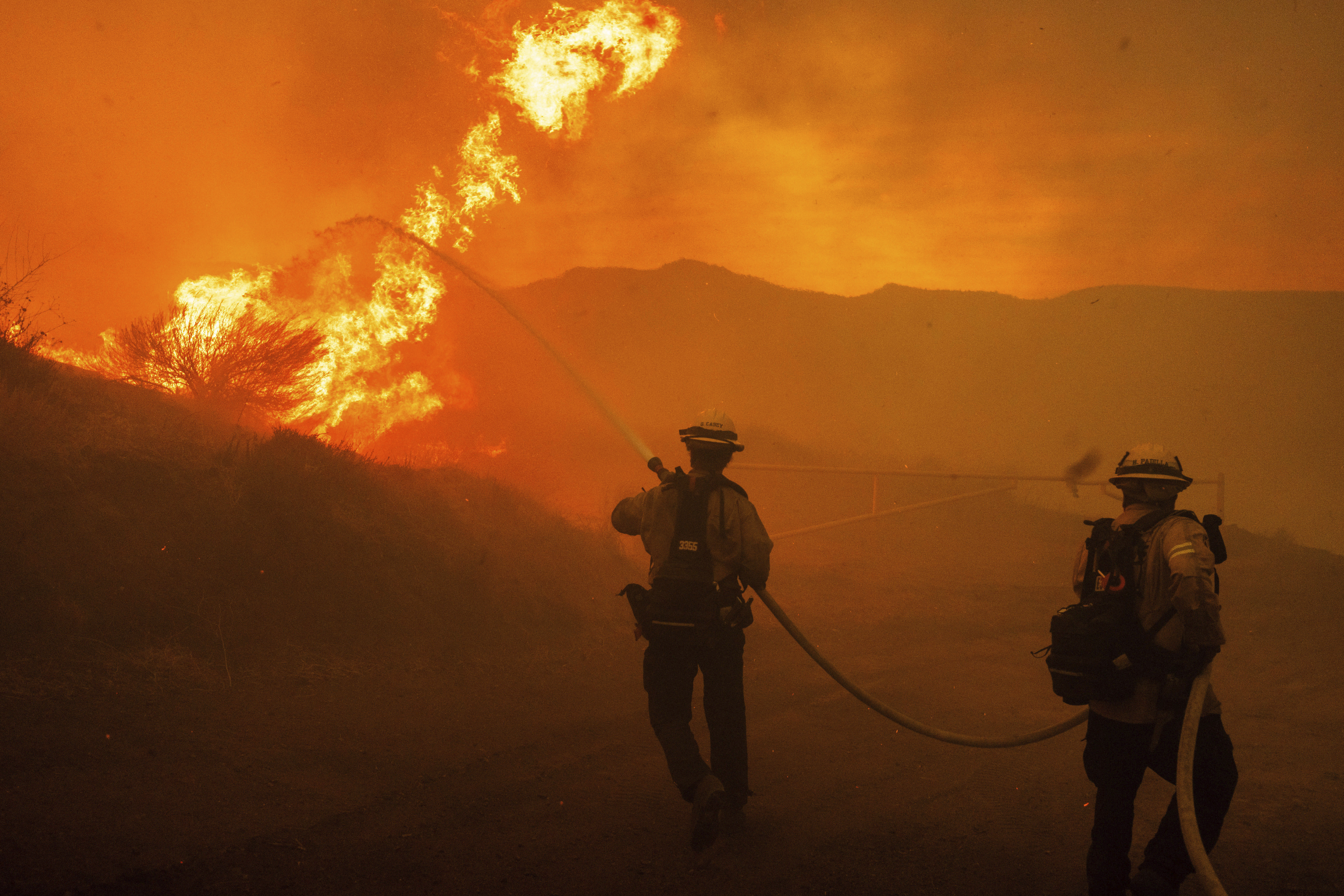 Firefighters spray water as they monitor flames caused by the Hughes Fire along a roadside in Castaic, Calif., Wednesday, Jan. 22, 2025. (AP Photo/Ethan Swope)