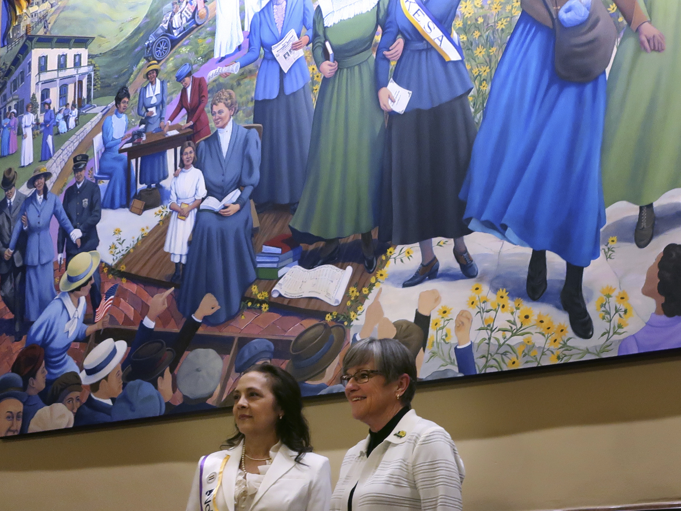 Artist Phyllis Garibay-Coon, left, and Kansas Gov. Laura Kelly, right, stand beneath Garibay-Coon's newly unveiled mural honoring Kansas women who campaigned for voting rights, Wednesday, Jan. 29, 2025, at the Statehouse in Topeka, Kan. (AP Photo/John Hanna)