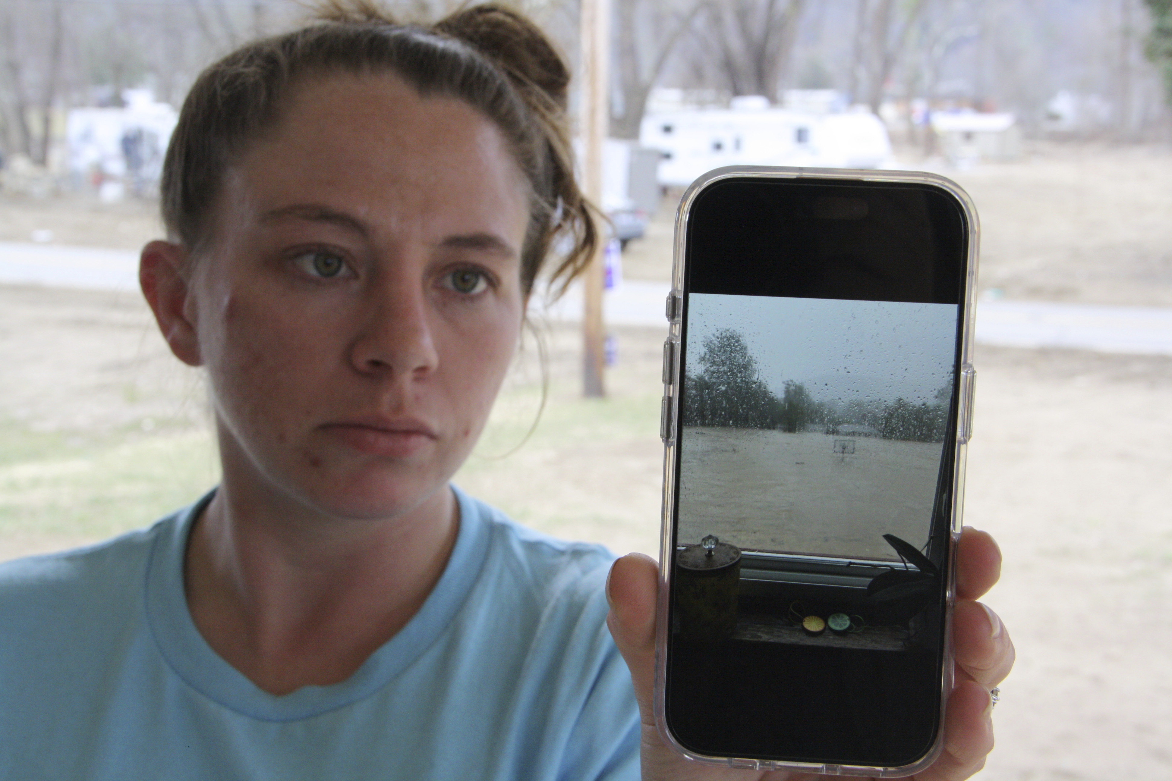 Emily Russell holds up her phone to show a photo of the previous flooding during Hurricane Helene outside her home in Swannanoa, N.C., on Thursday, Feb. 6, 2025. (AP Photo/Makiya Seminera)